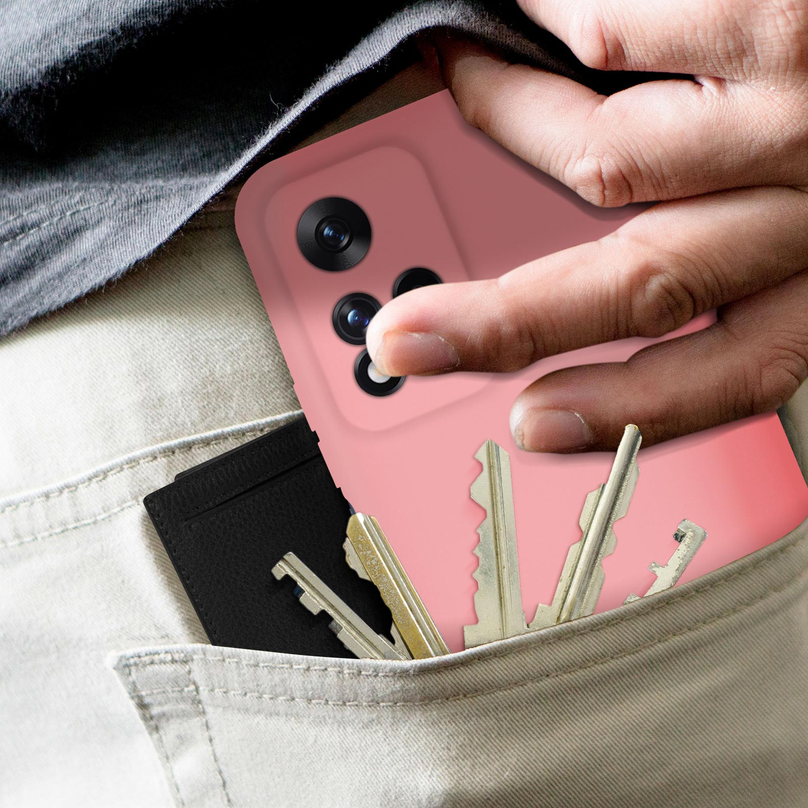 Mano in tasca che tiene un telefono rosa. Chiavi e porta carte nero in tasca.