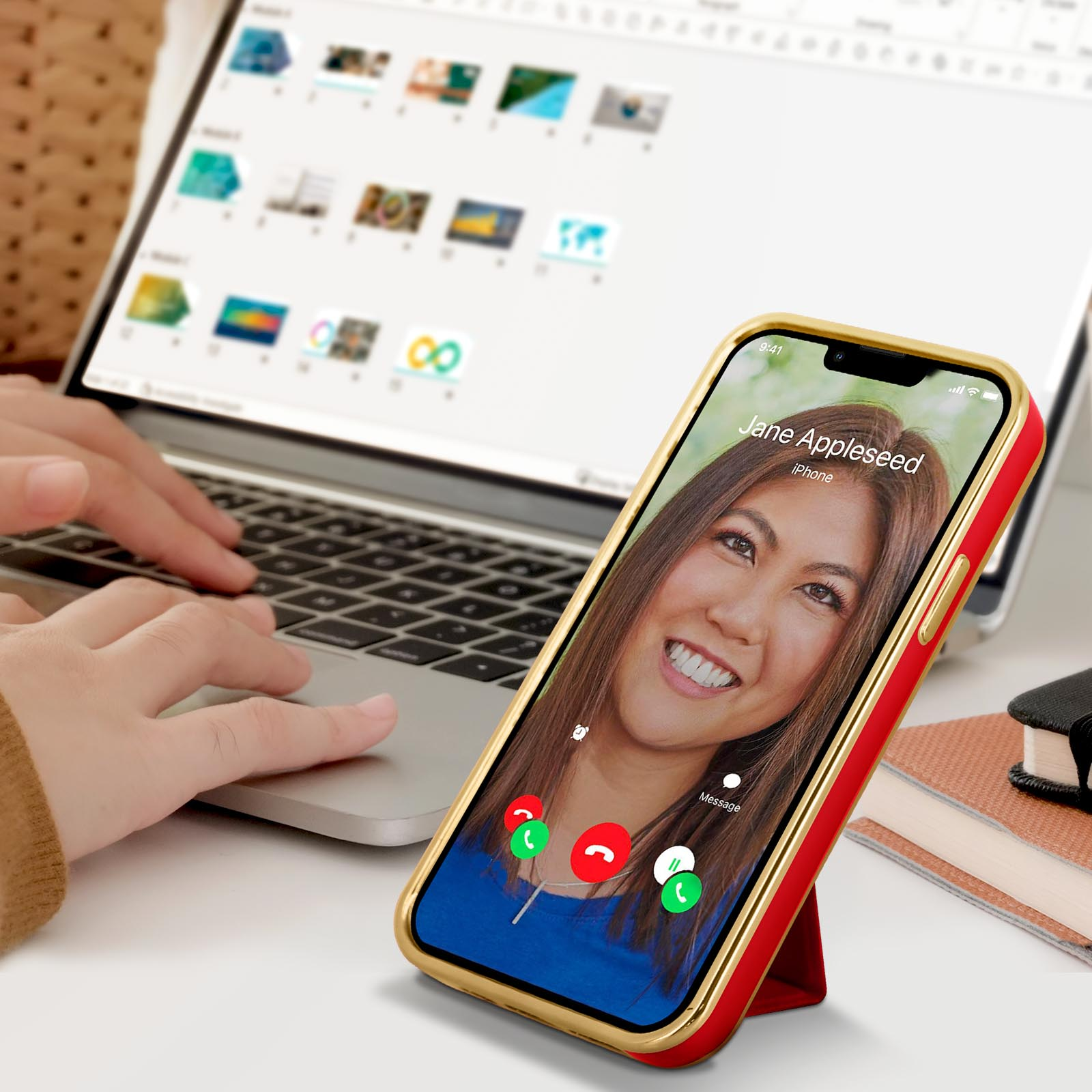 Telefono su supporto, videochiamata. Custodia rossa e oro. Donna sorridente sullo schermo. Laptop sullo sfondo.