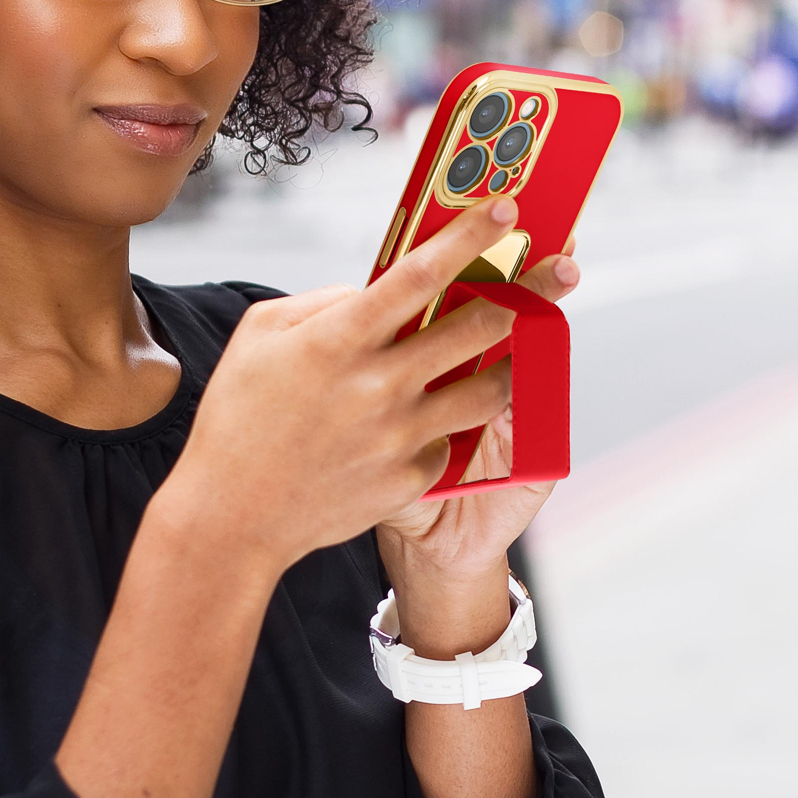 Donna che tiene un telefono rosso con custodia e supporto dorati. Indossa un orologio bianco.