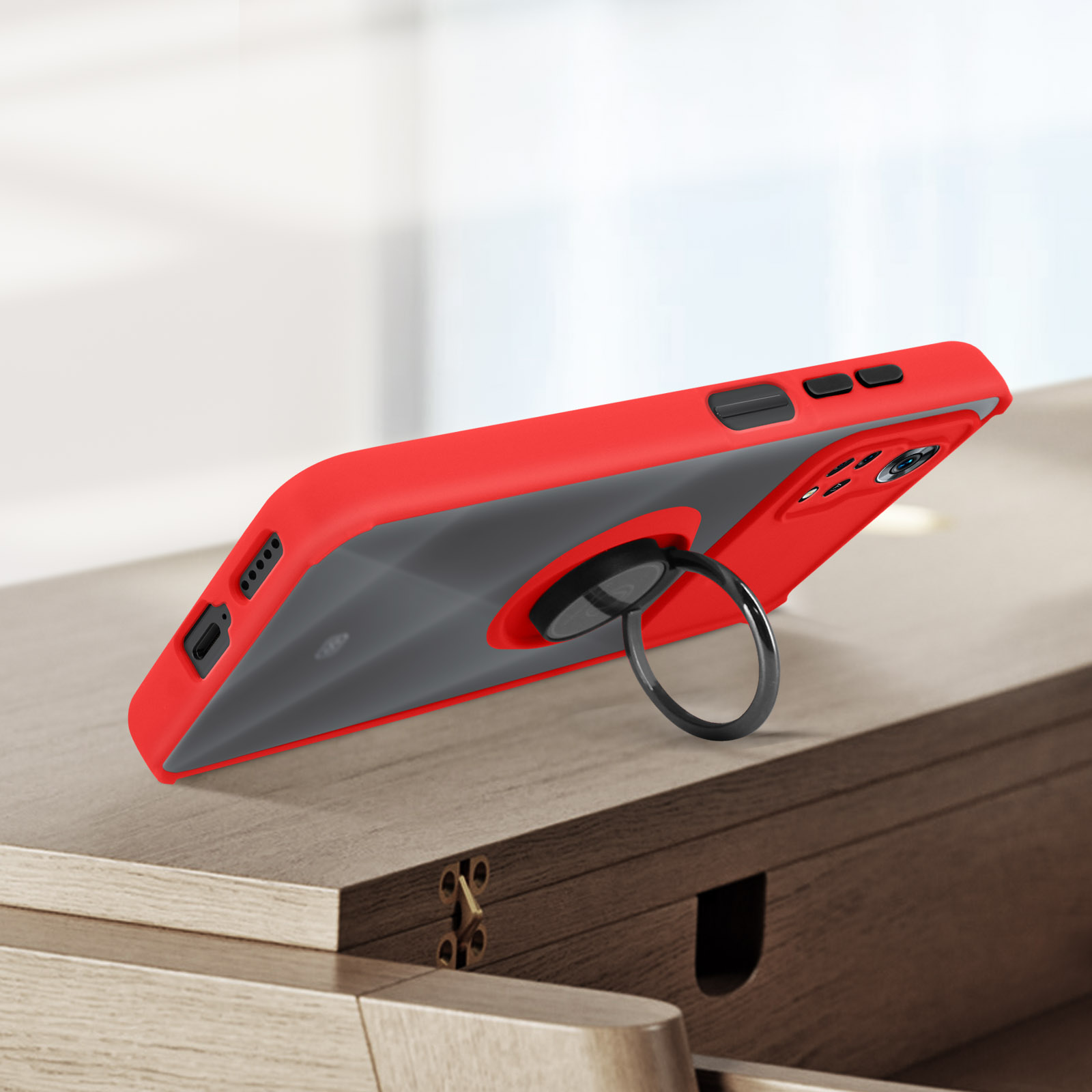 Coque de téléphone rouge et grise avec anneau. Le téléphone est sur un meuble en bois. Le côté est net.