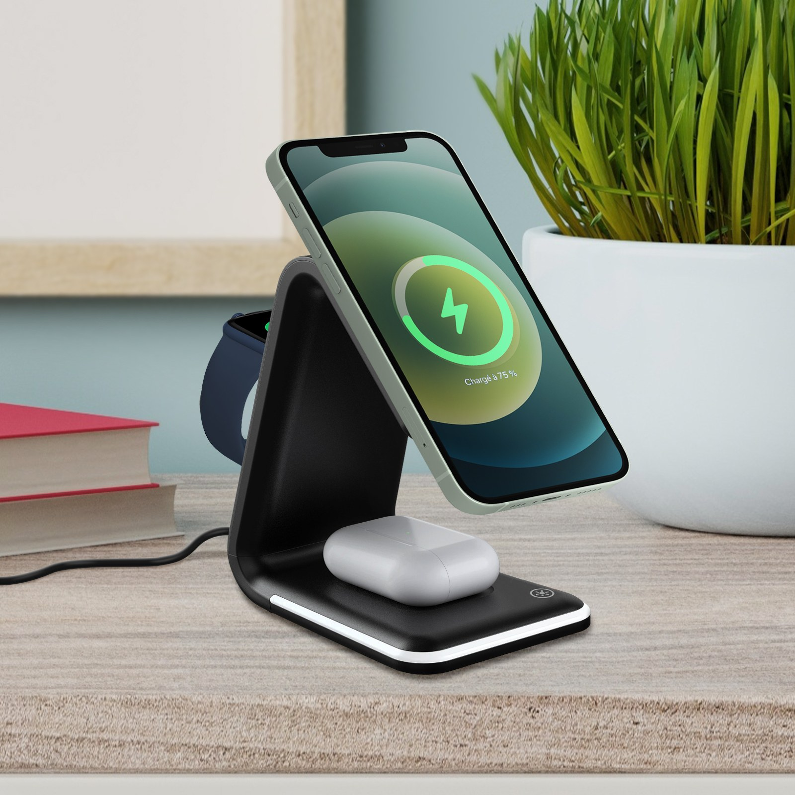 Eine schwarze Ladestation mit Telefon, Uhr und AirPods. Das Telefon zeigt ein Ladesymbol. Pflanze im Hintergrund.