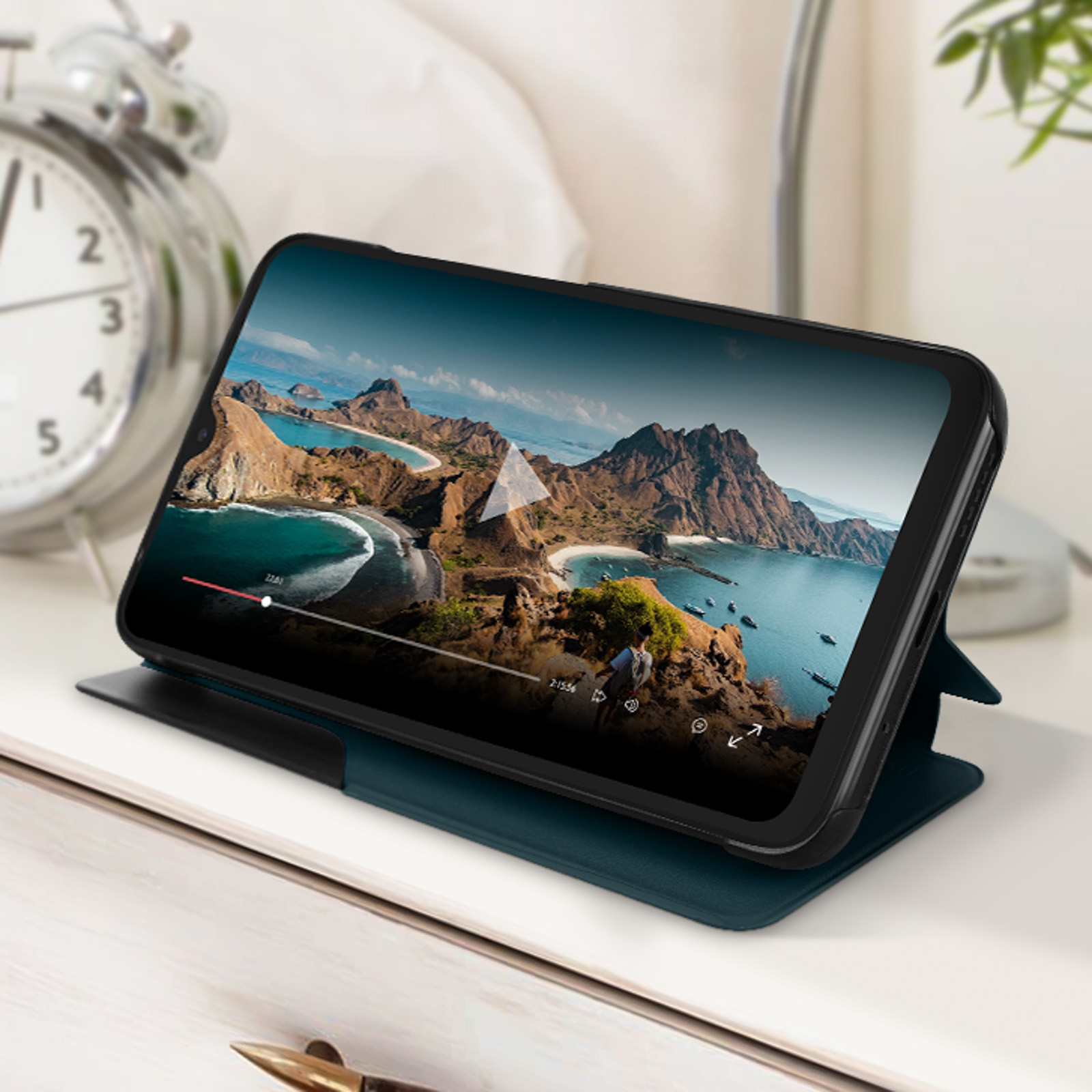 Telefono su supporto che mostra un paesaggio. Orologio e letto sullo sfondo.