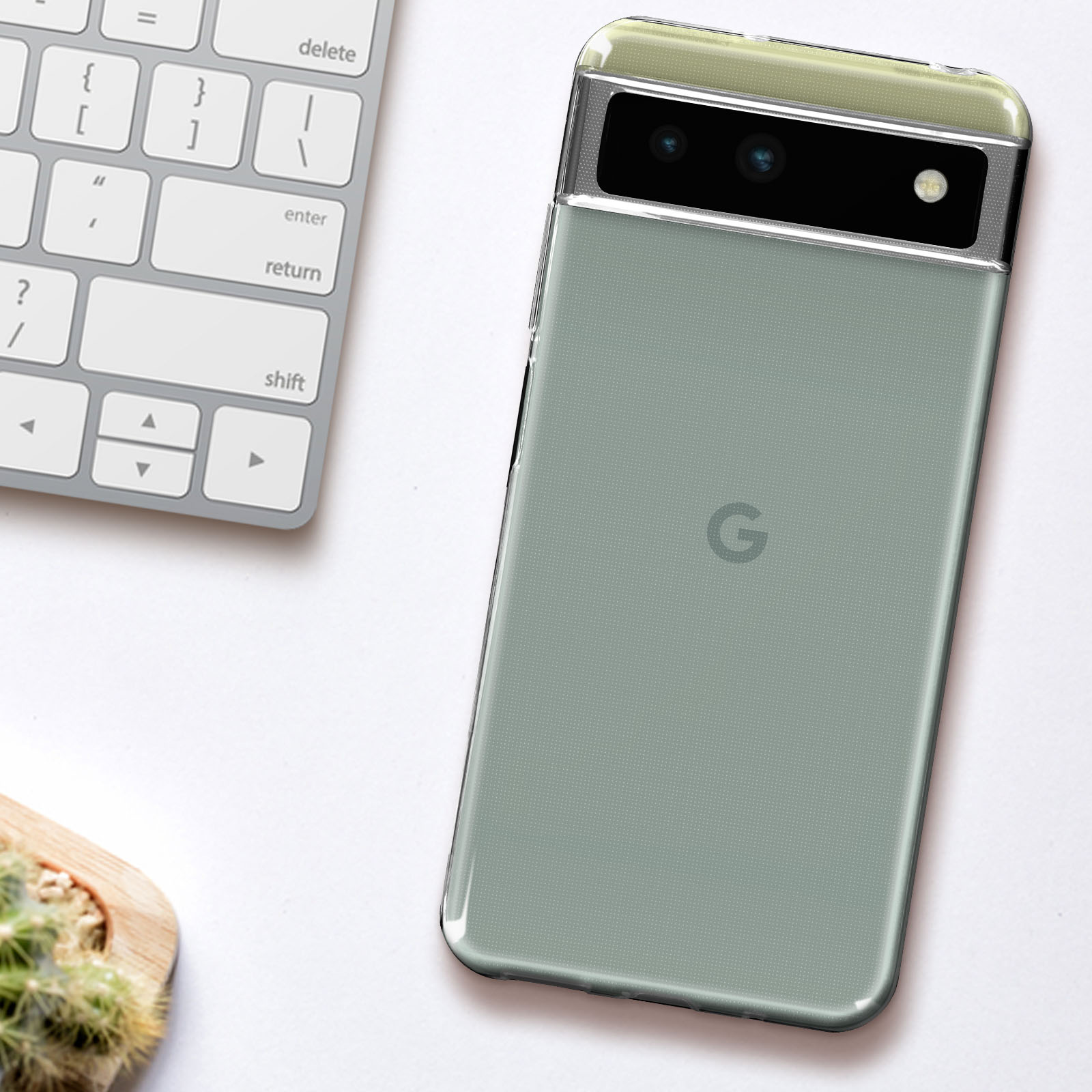 Een telefoon in een groen getinte hoes. De telefoon ligt op een witte ondergrond, naast een toetsenbord en een kleine cactus.