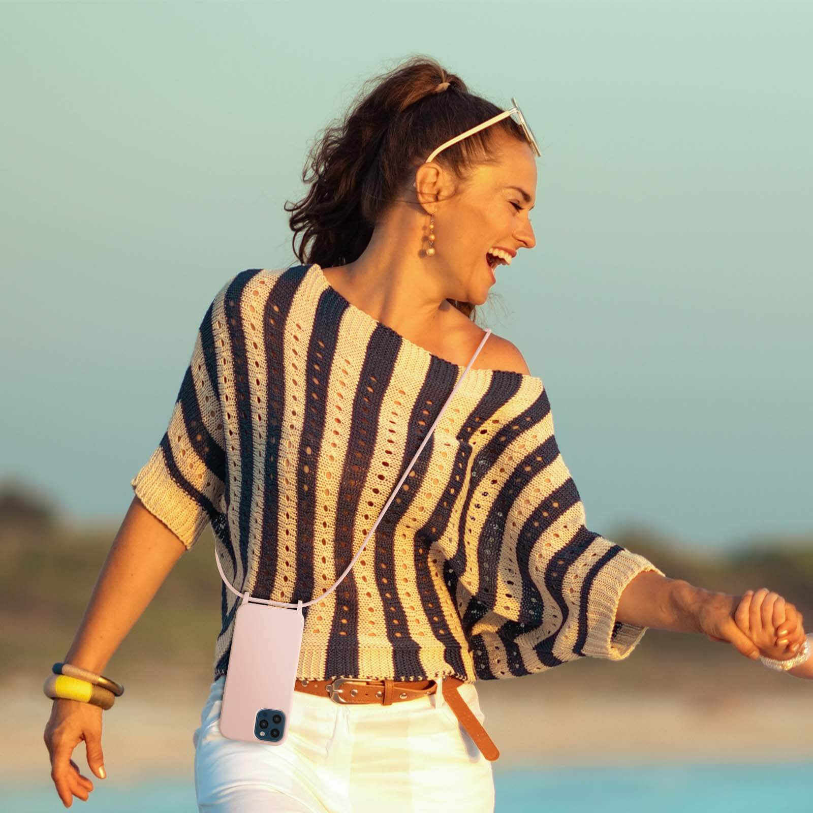 Une femme en chemise rayée tient un téléphone rose avec un cordon sur une plage.