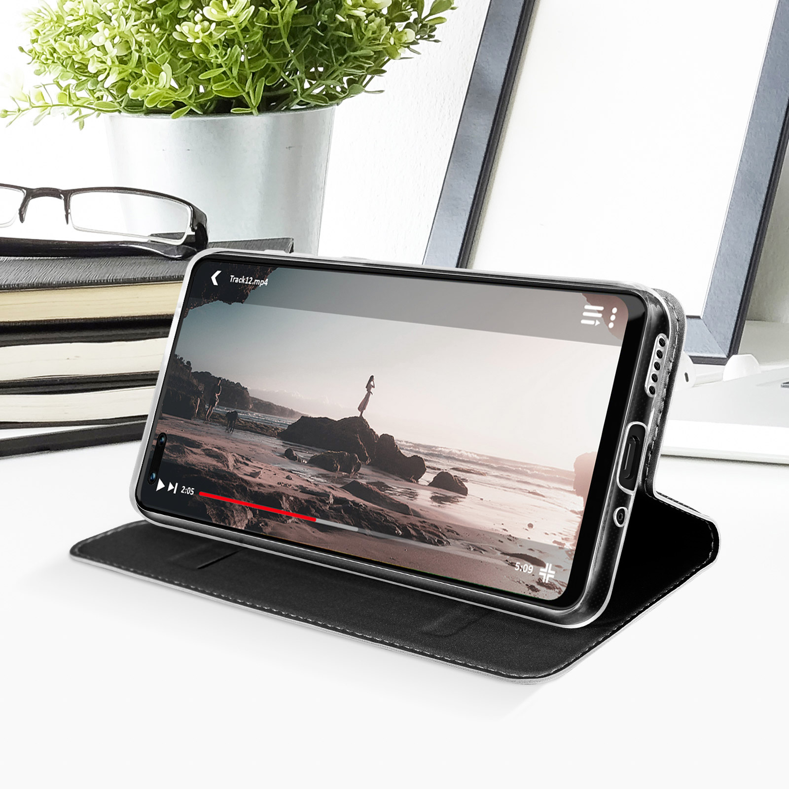 Telefono in una custodia, riproduce un video. Libri e occhiali sullo sfondo.