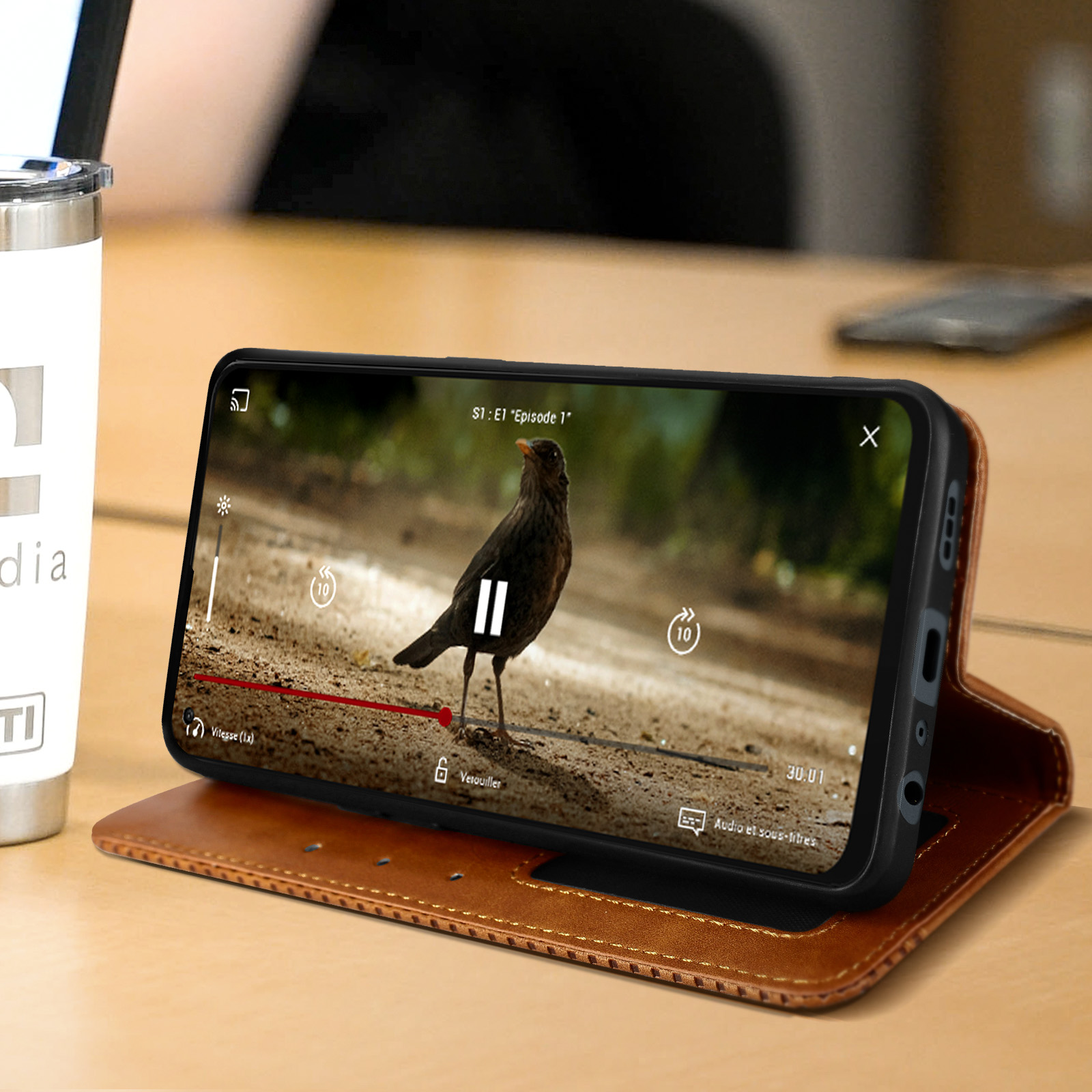 Un telefono su un supporto, che mostra un video di un uccello. Una tazza bianca è accanto.