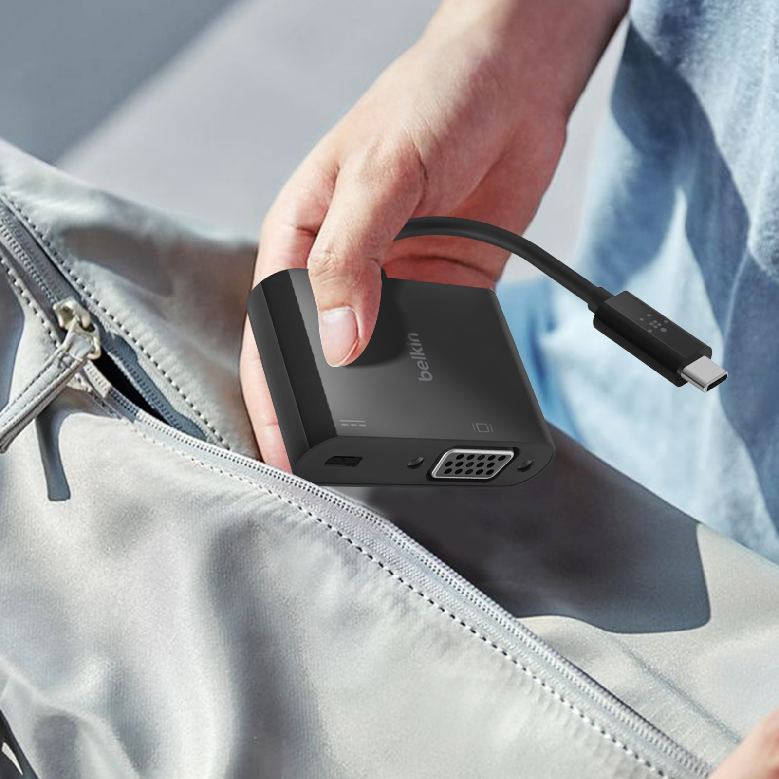 Adattatore Belkin nero con cavo USB-C, tenuto in mano. Sfondo grigio.