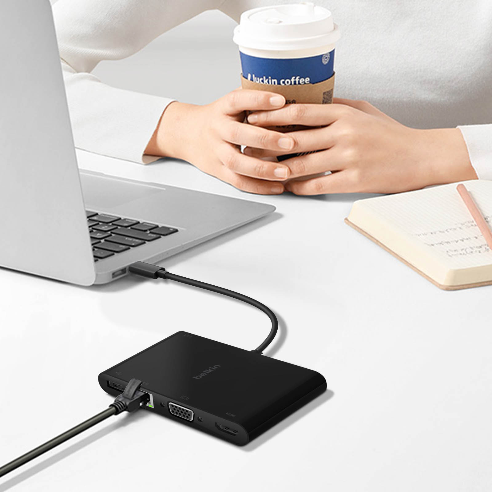 Adattatore Belkin nero collegato al laptop. Tazza di caffè e taccuino sulla scrivania.