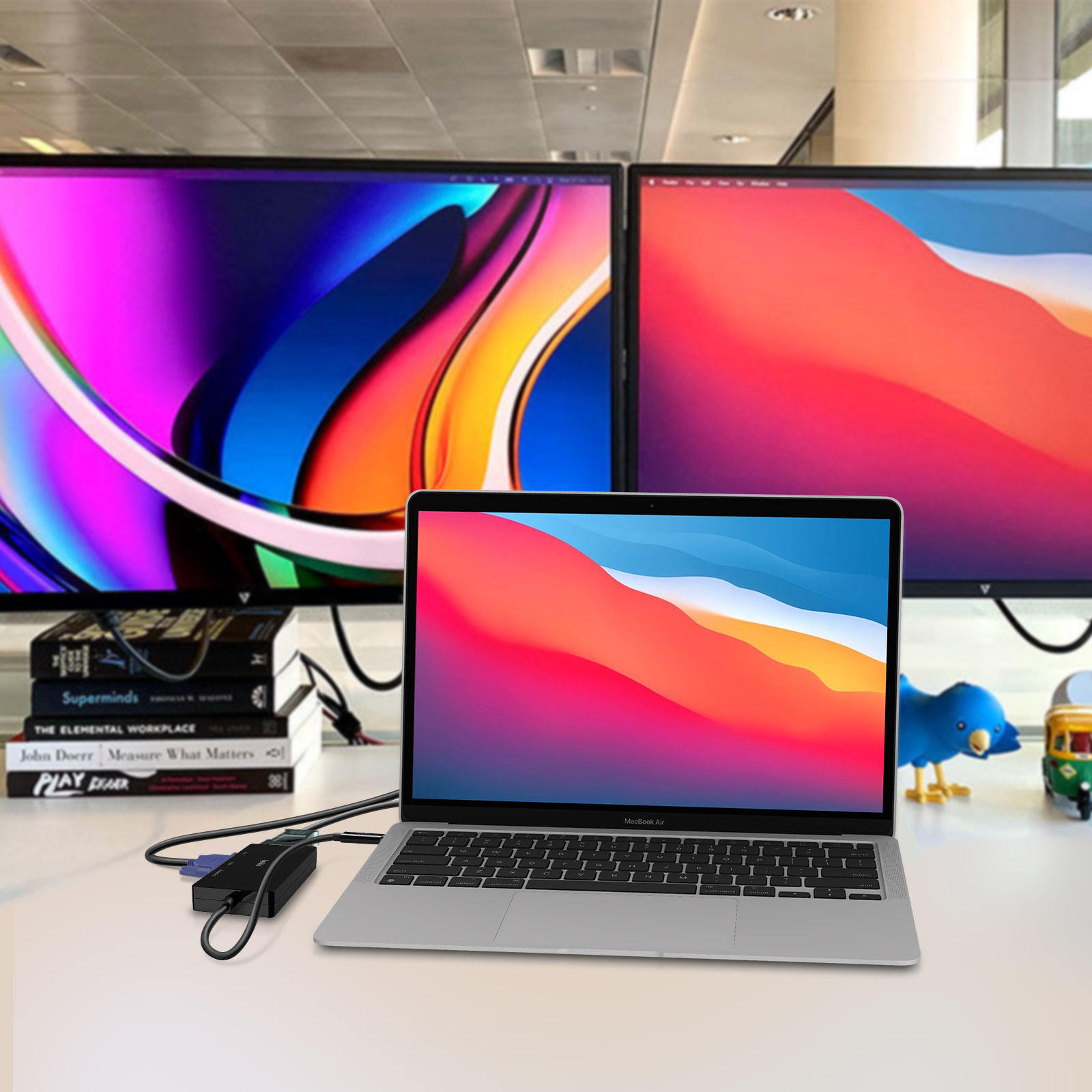 Laptop, due monitor e altri oggetti da ufficio su una scrivania. Lo sfondo è un muro.