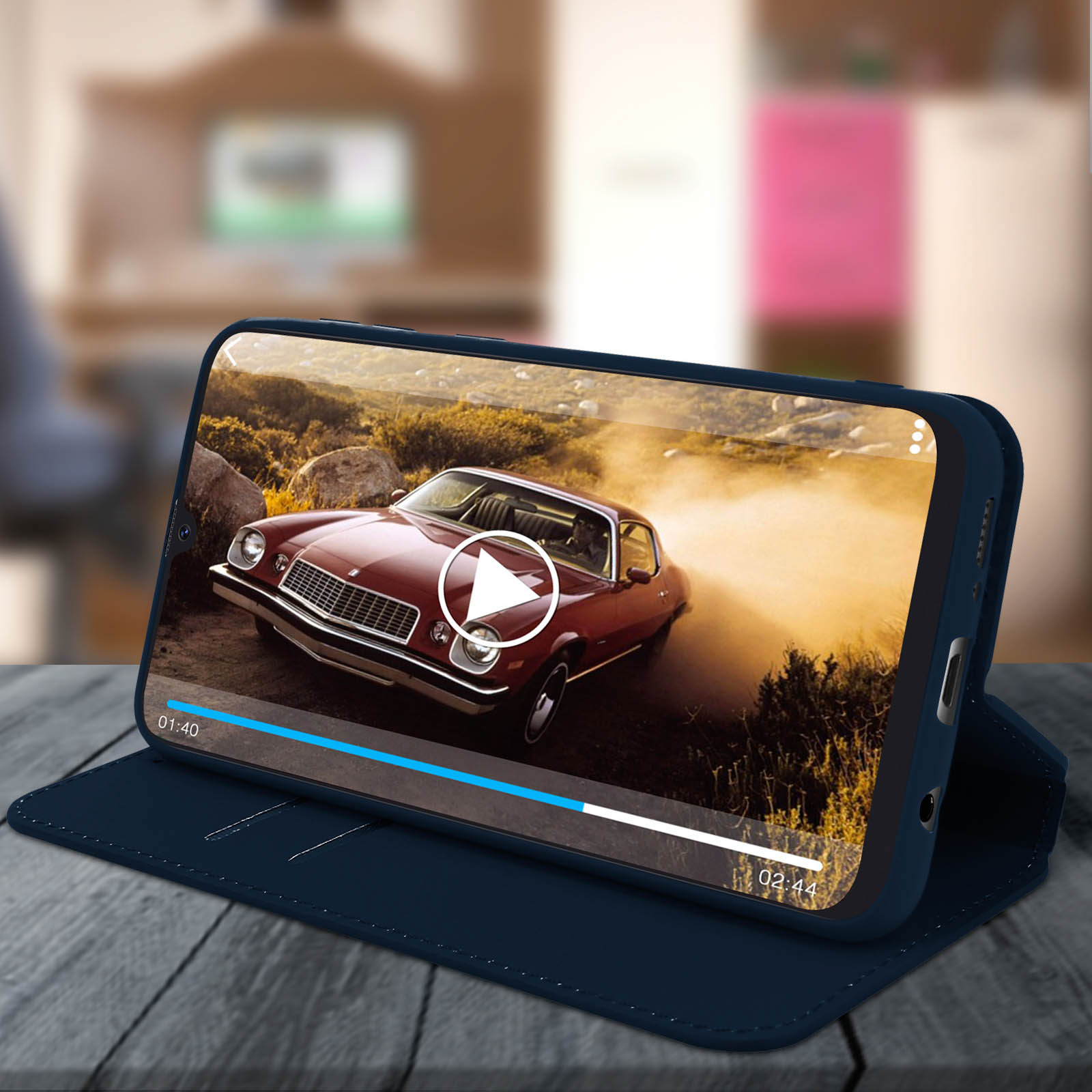 Smartphone in custodia blu mostra video di auto rossa con pulsante play su superficie legno.