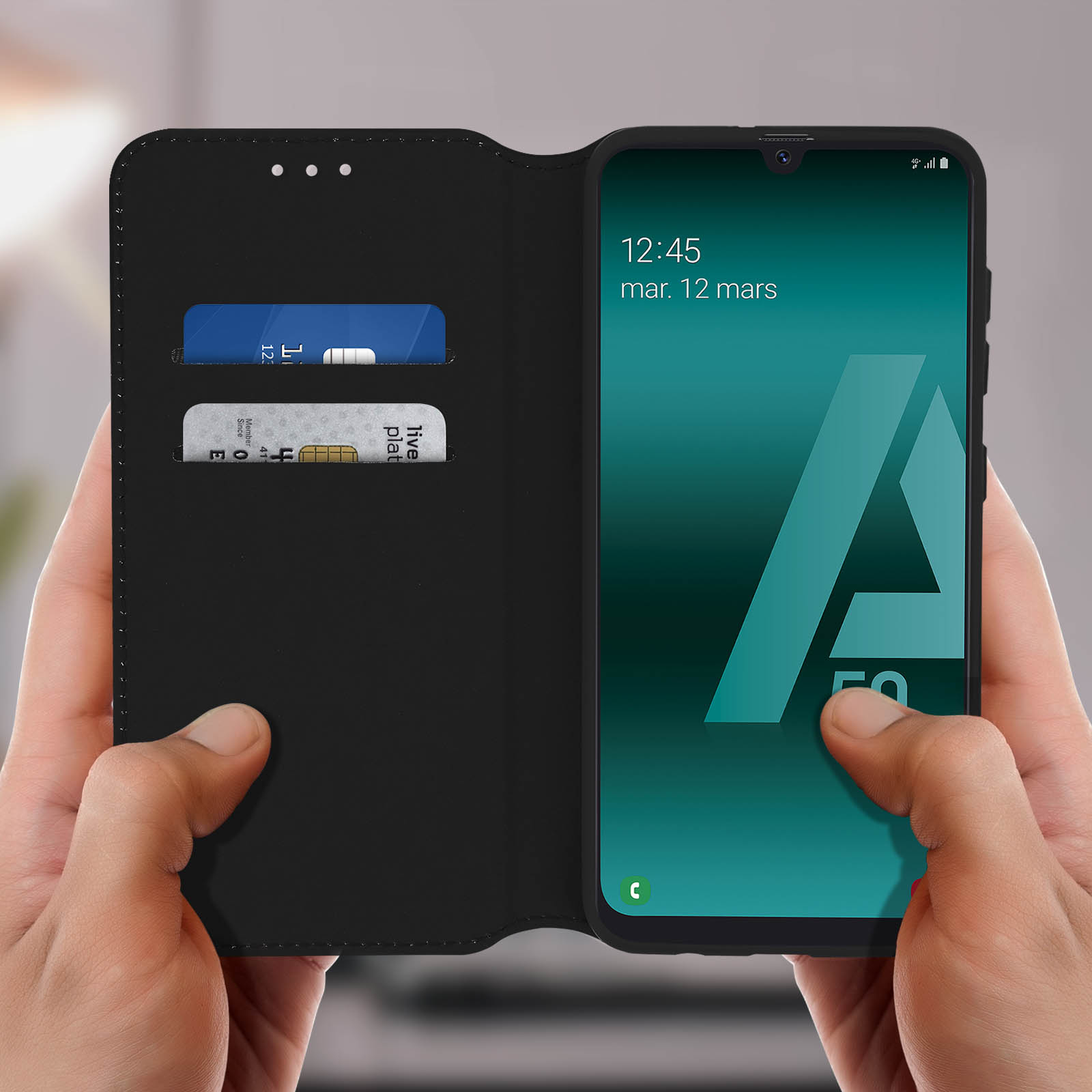 Una persona che tiene un telefono con una custodia nera, che mostra l'ora e gli slot per le carte.