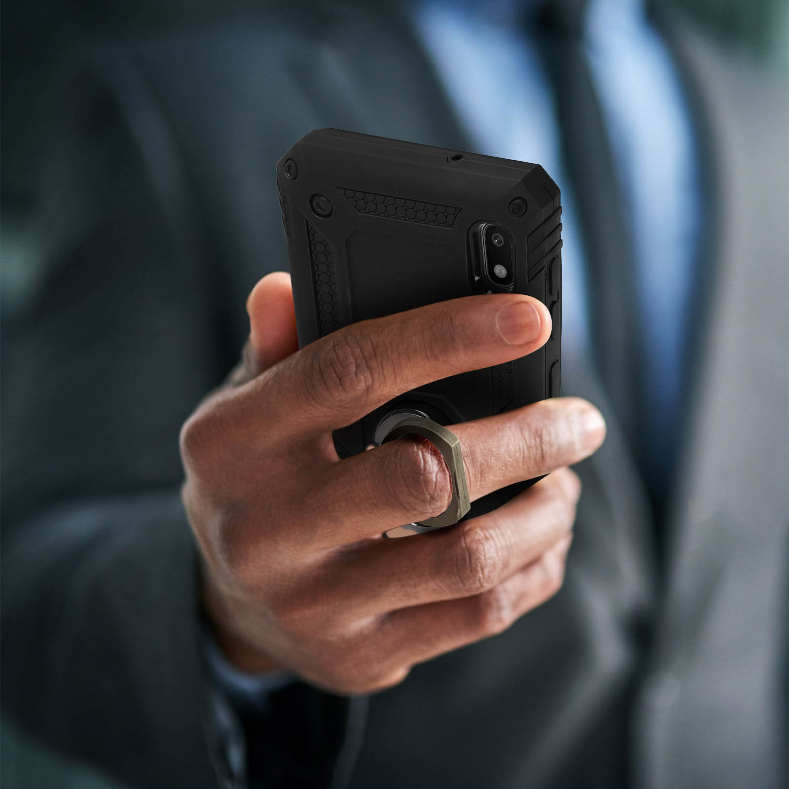 Main tenant un téléphone noir avec anneau. Personne en costume. Arrière-plan flou, type bureau.