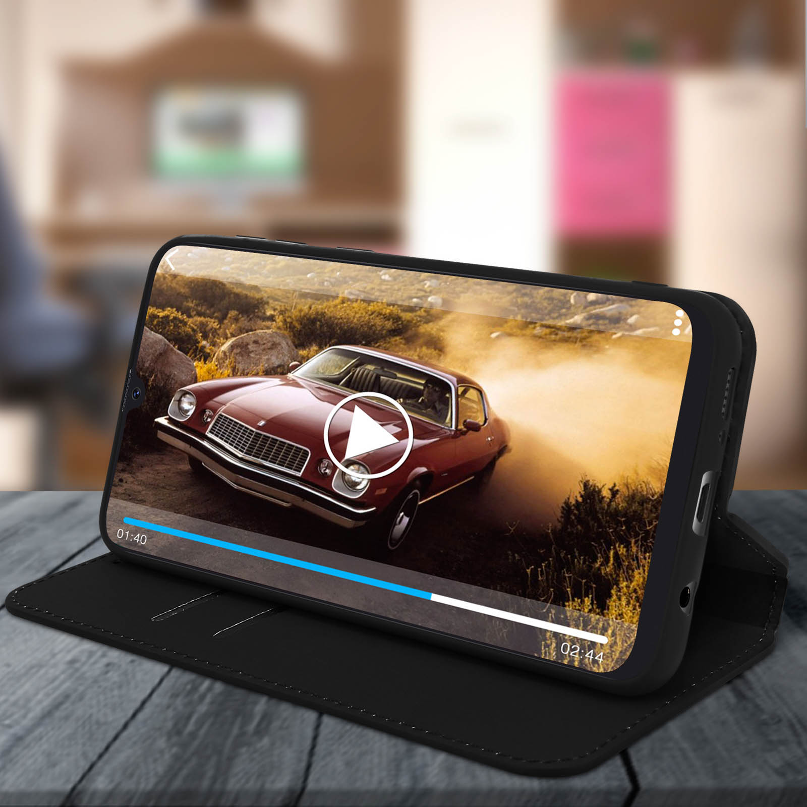 Telefono in custodia nera che mostra un video, appoggiato. Custodia nera su superficie nera, sfondo sfocato.