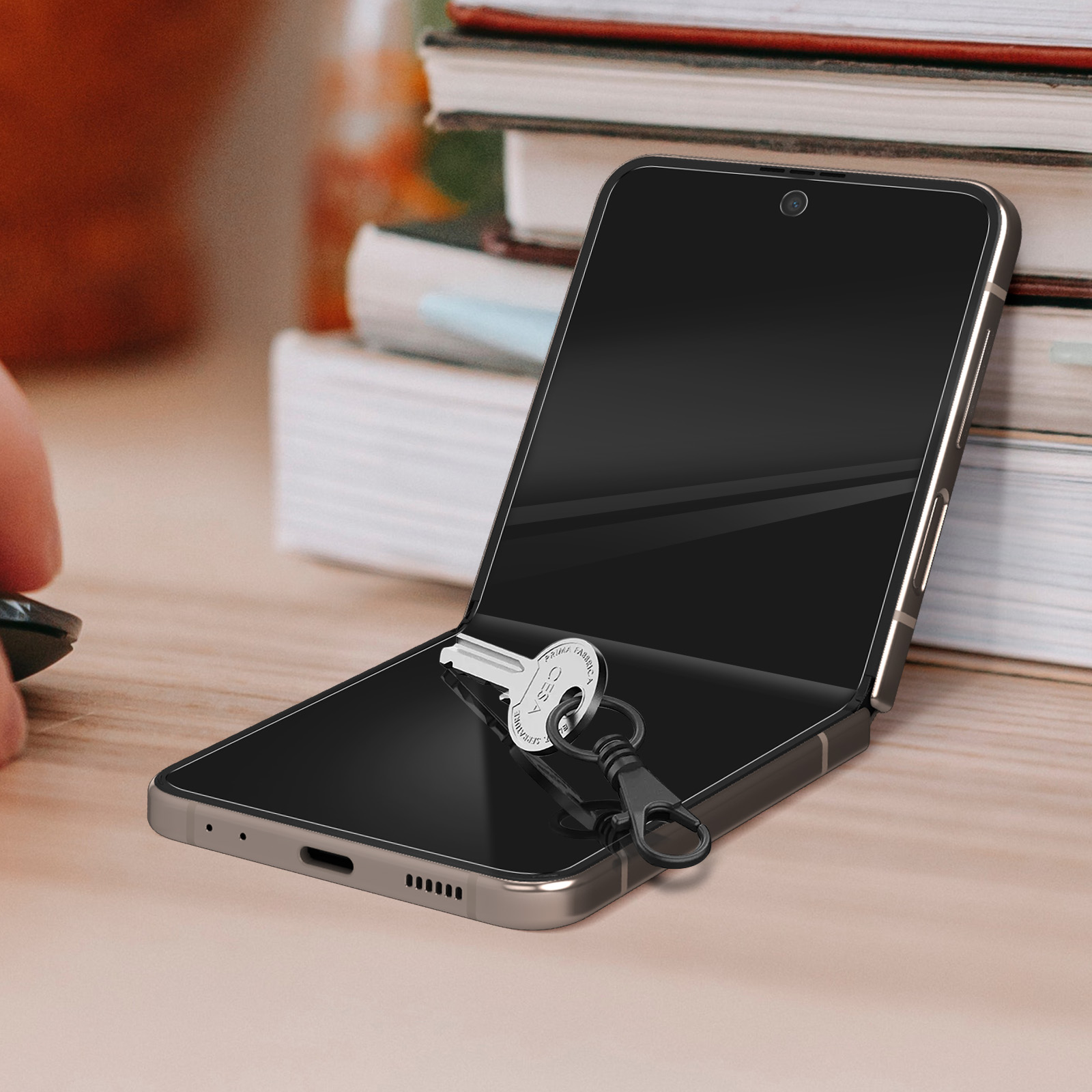 Un téléphone pliable ouvert avec une clé attachée. Sur une table, avec une main dans le coin.