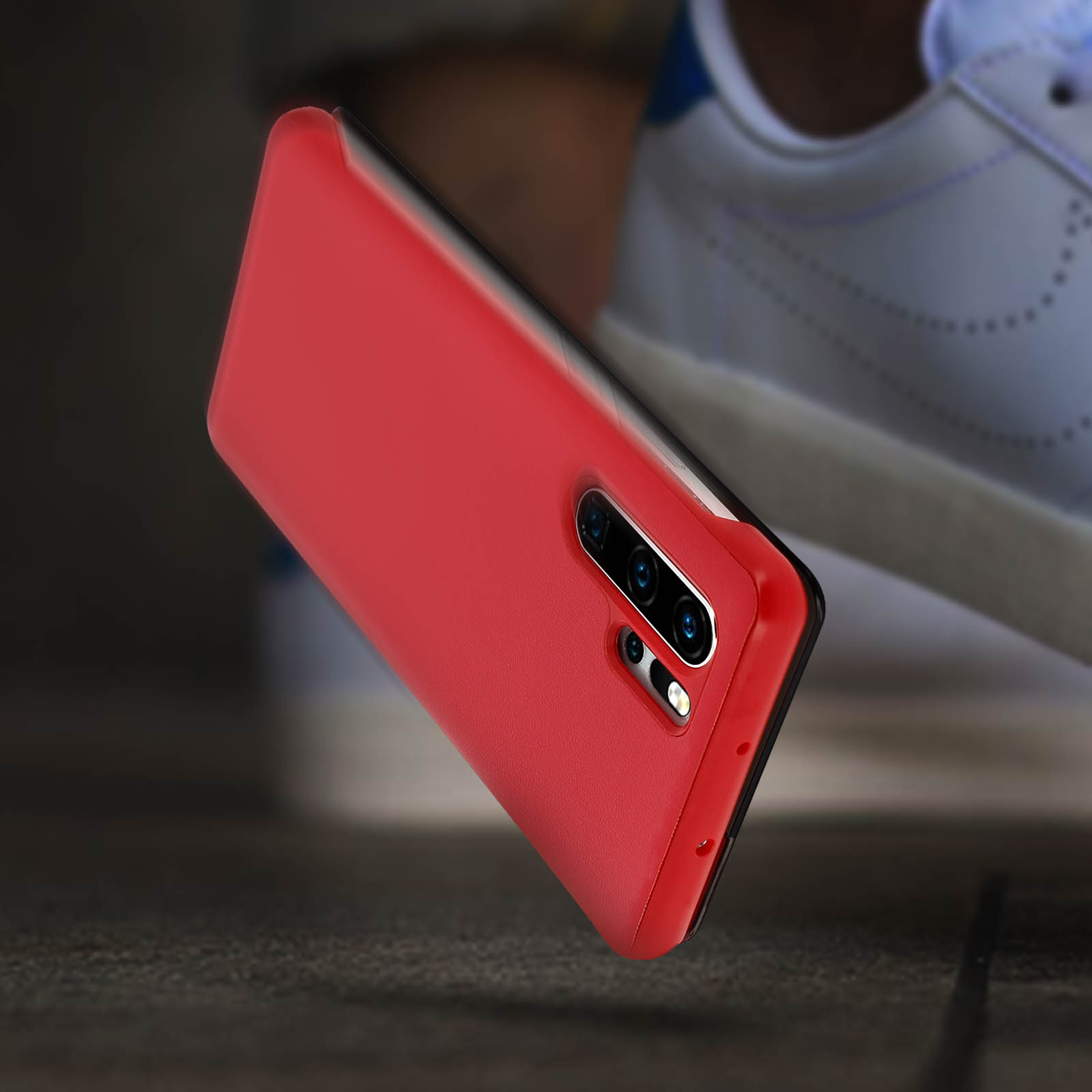 Custodia rossa per telefono che cade con il telefono all'interno. Sfondo chiaro con particelle di polvere.