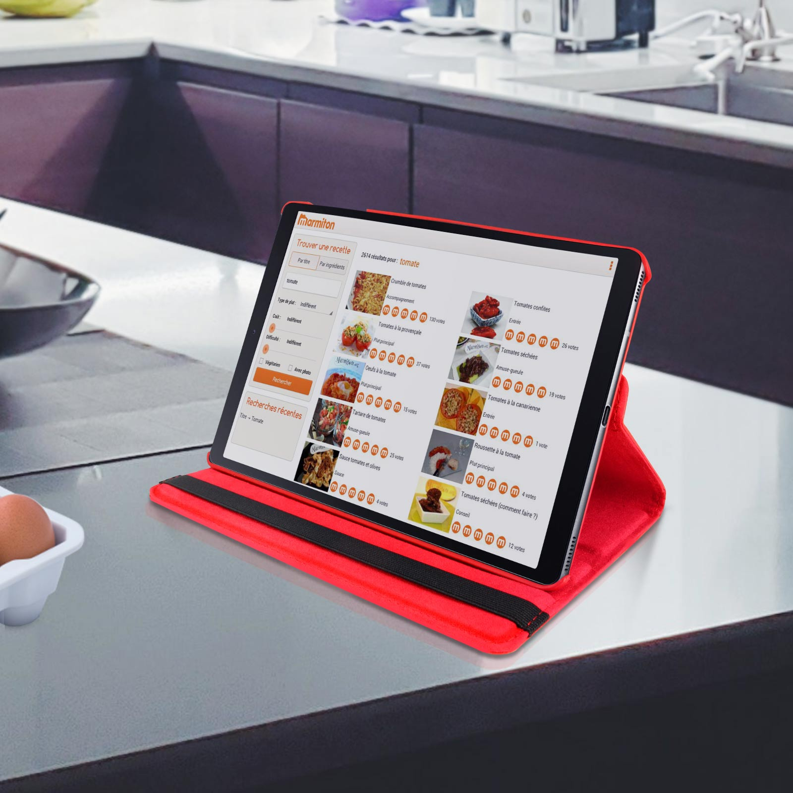 Tablet rosso in custodia rossa. Il display mostra ricette. Tavolo e piano di lavoro in metallo visibili.