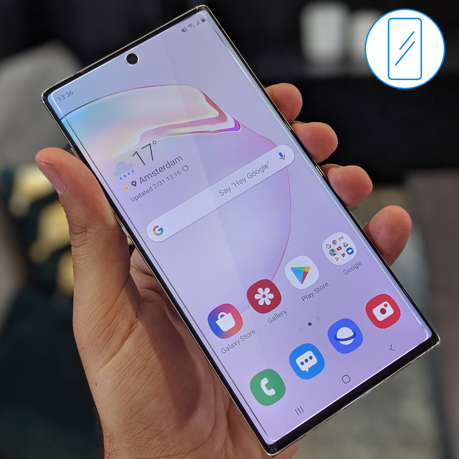 Una mano tiene in mano un telefono che mostra la schermata iniziale con icone delle app e ora/data. Sfondo sfocato.