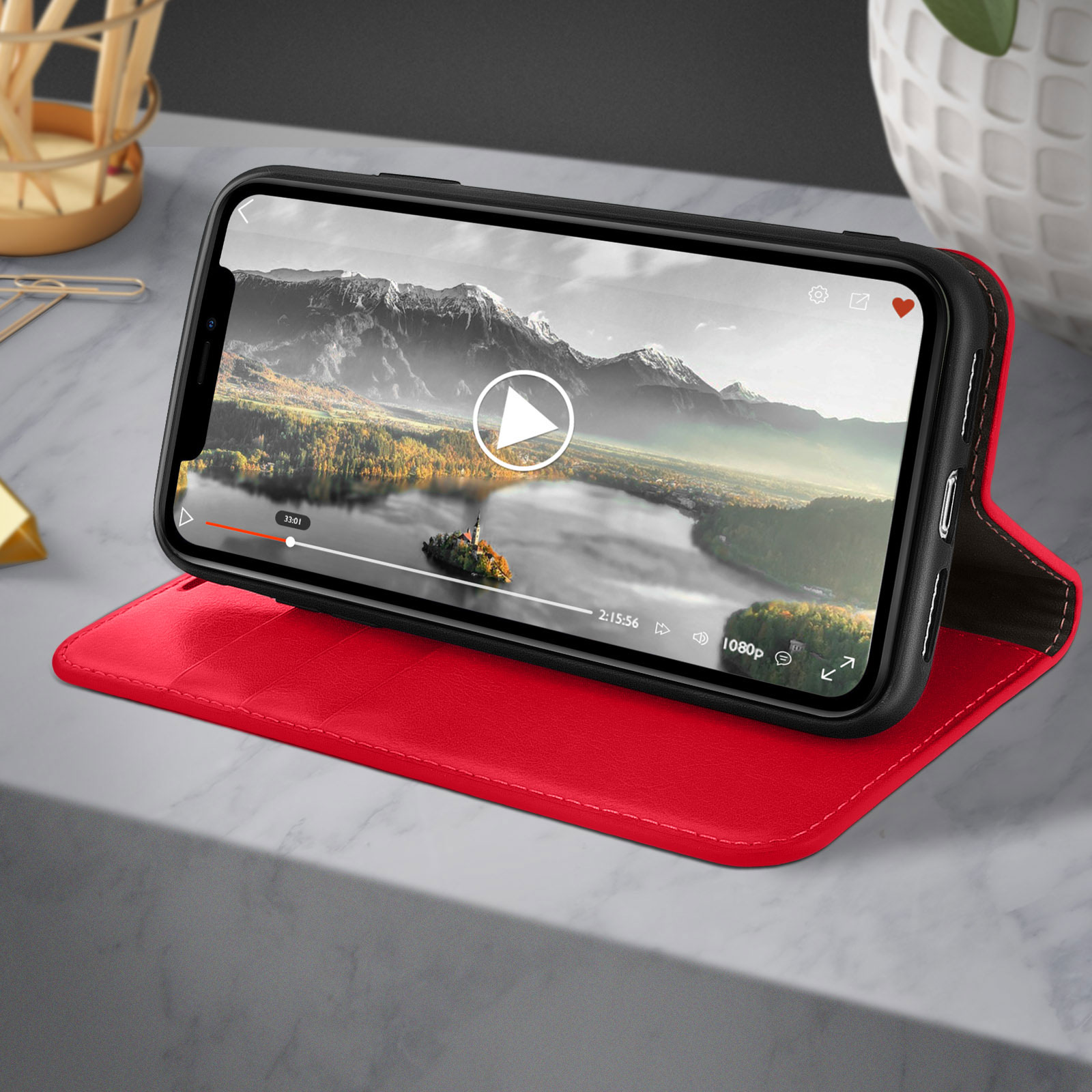 Een telefoon in een rode leren hoes toont een video op een marmeren oppervlak.