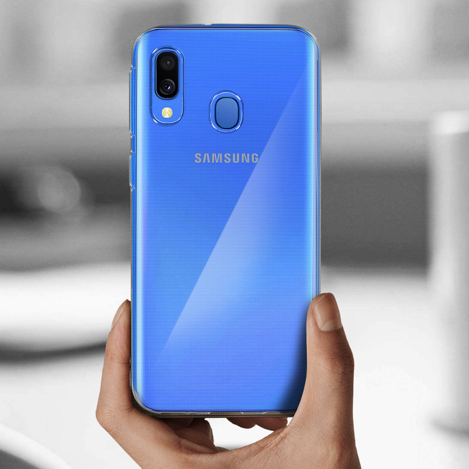 Una mano tiene in mano un telefono blu con una custodia trasparente. Il retro del telefono è visibile, con un logo Samsung.