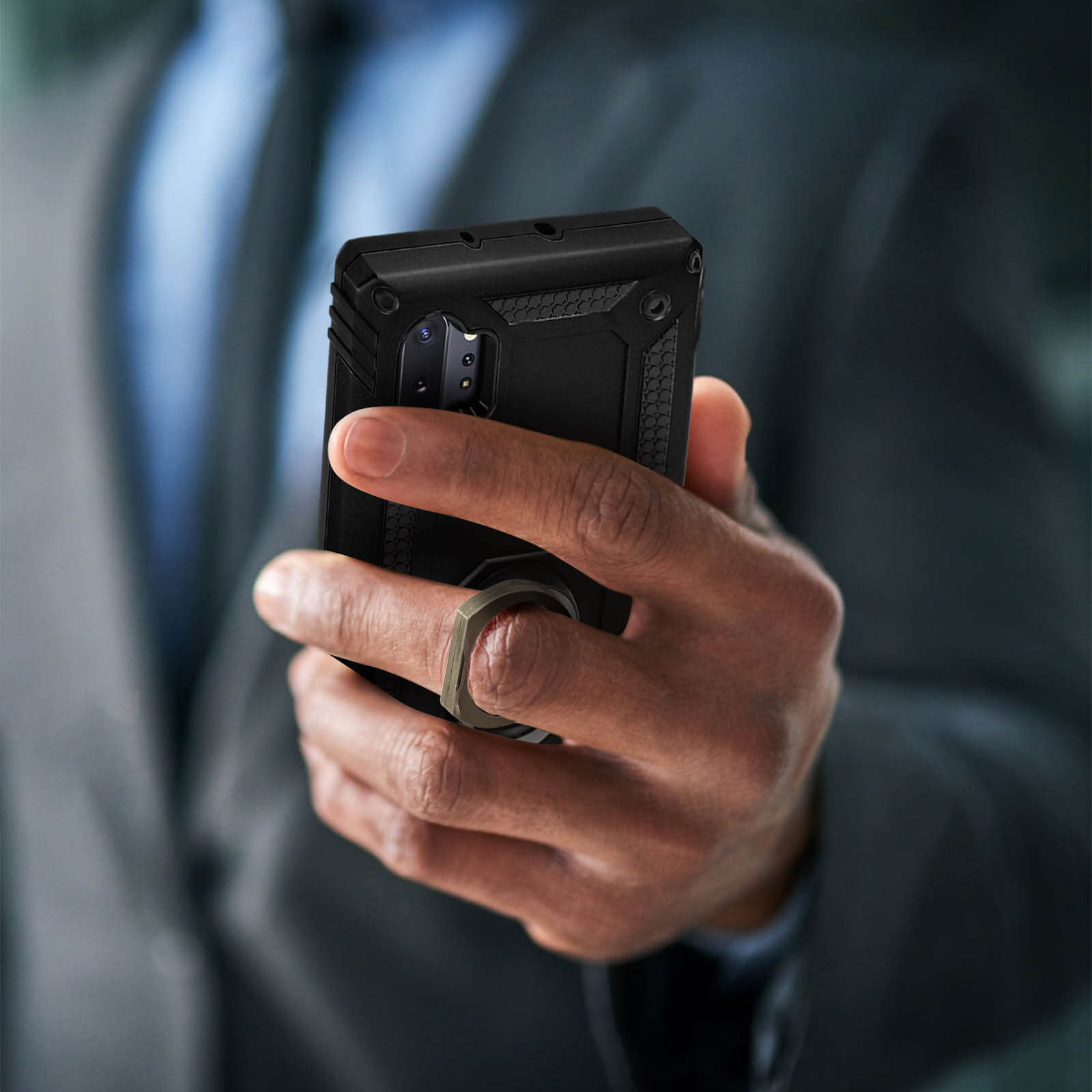 Een hand die een zwarte telefoon vasthoudt. De telefoon heeft een metalen ring aan de achterkant.