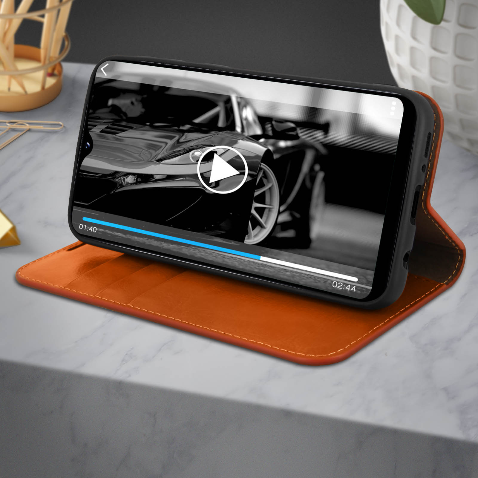Ein Telefon, das ein Video mit einem schwarzen Auto auf dem Bildschirm abspielt, auf einer orangefarbenen Handyhülle.