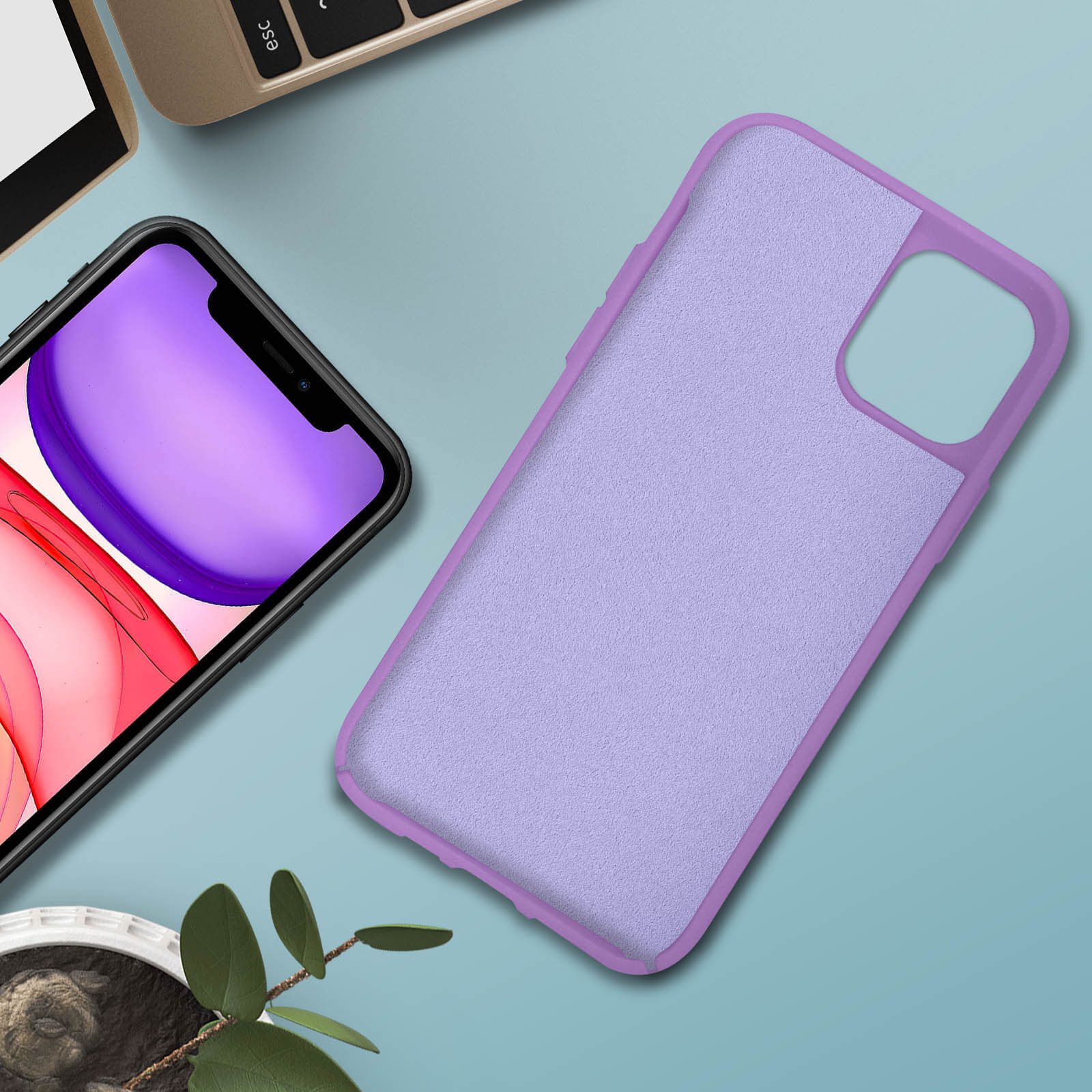Lila telefoonhoesje op een blauw oppervlak. Zwarte telefoon ernaast. Groene plant en laptop zijn ook aanwezig.