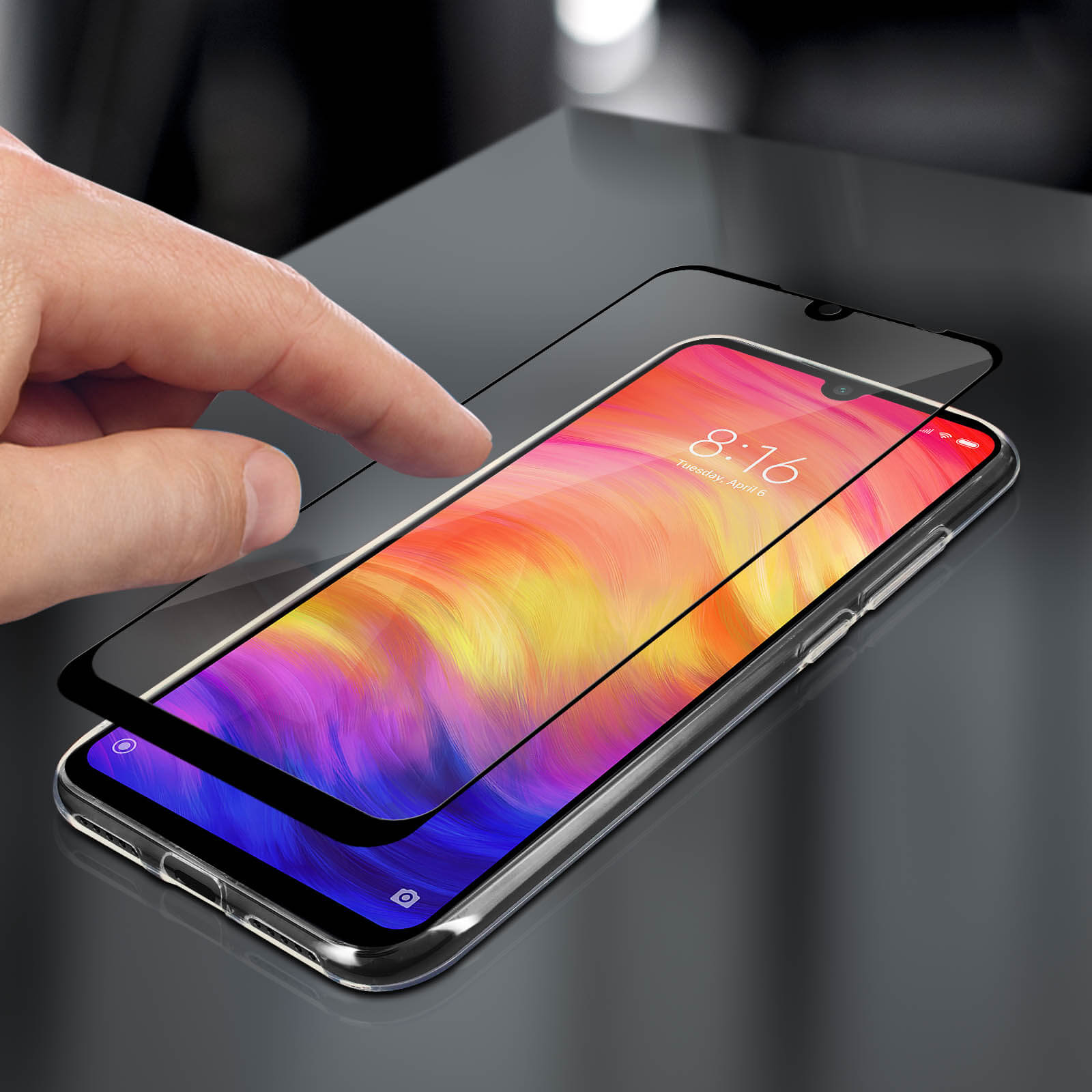 Mano che applica una protezione per lo schermo a un telefono. Il telefono mostra un display colorato. Superficie nera.