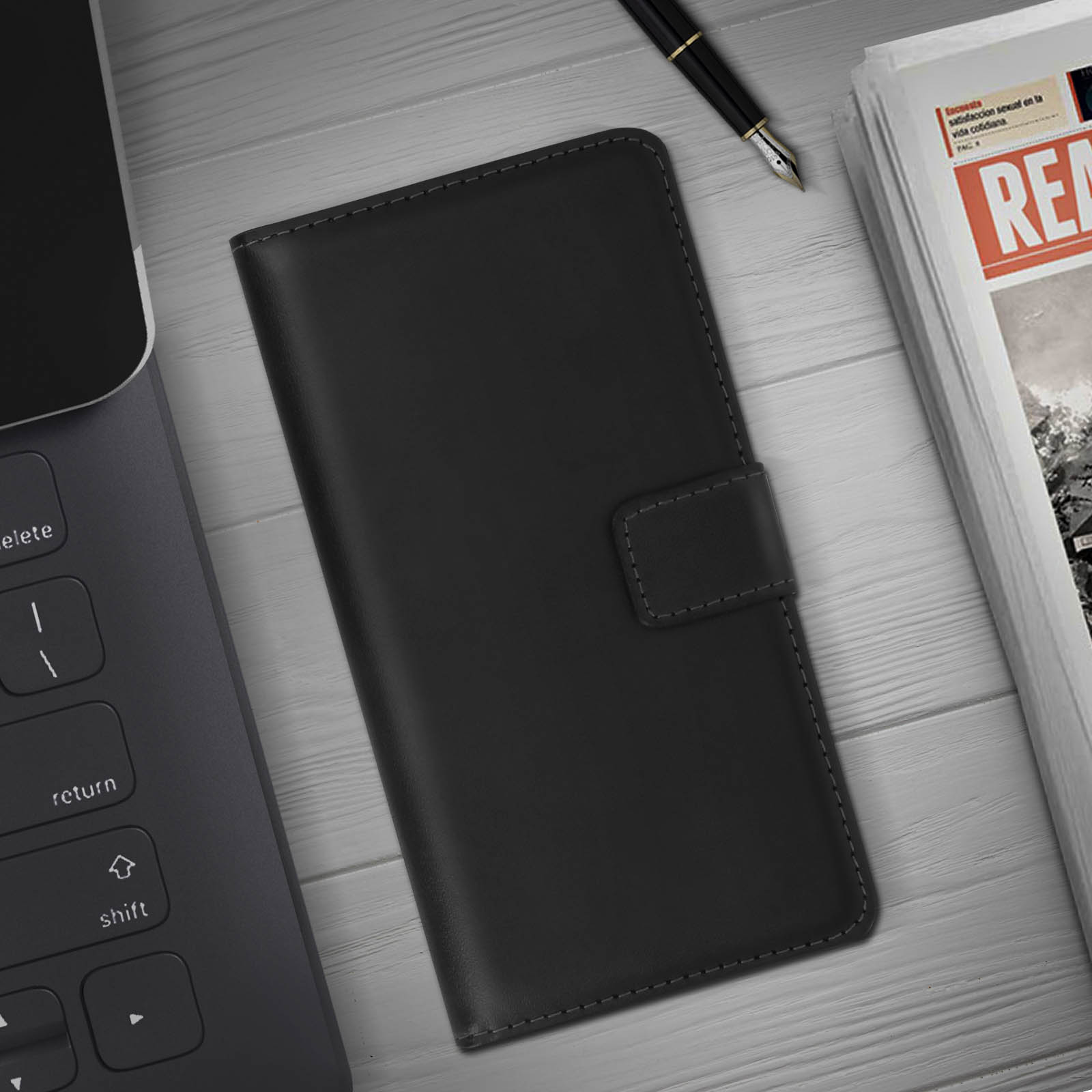 Custodia per telefono nera su una superficie di legno. Penna e giornale sullo sfondo. Custodia chiusa, con chiusura.
