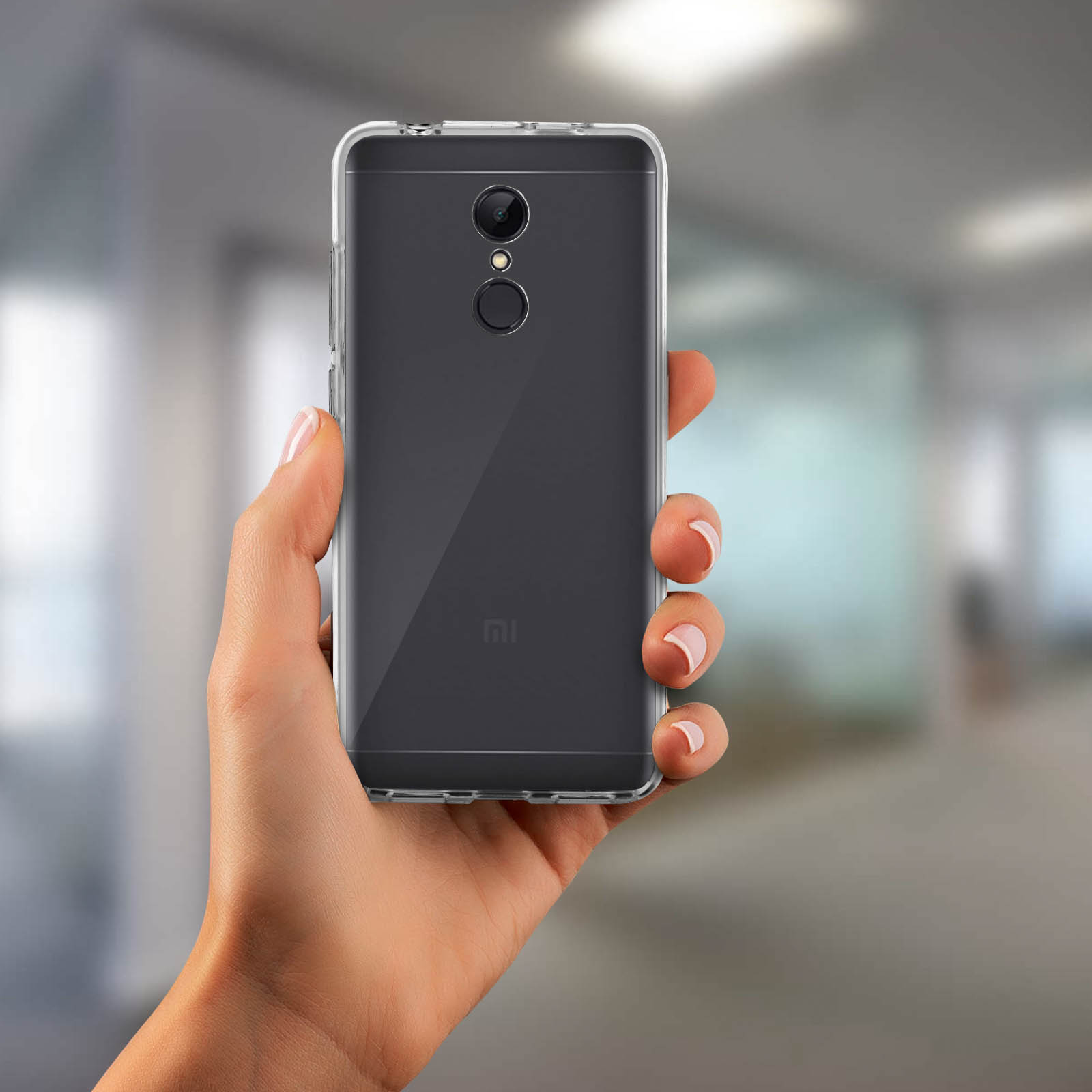 Mano sosteniendo un smartphone en una funda transparente. Fondo borroso, oficina.
