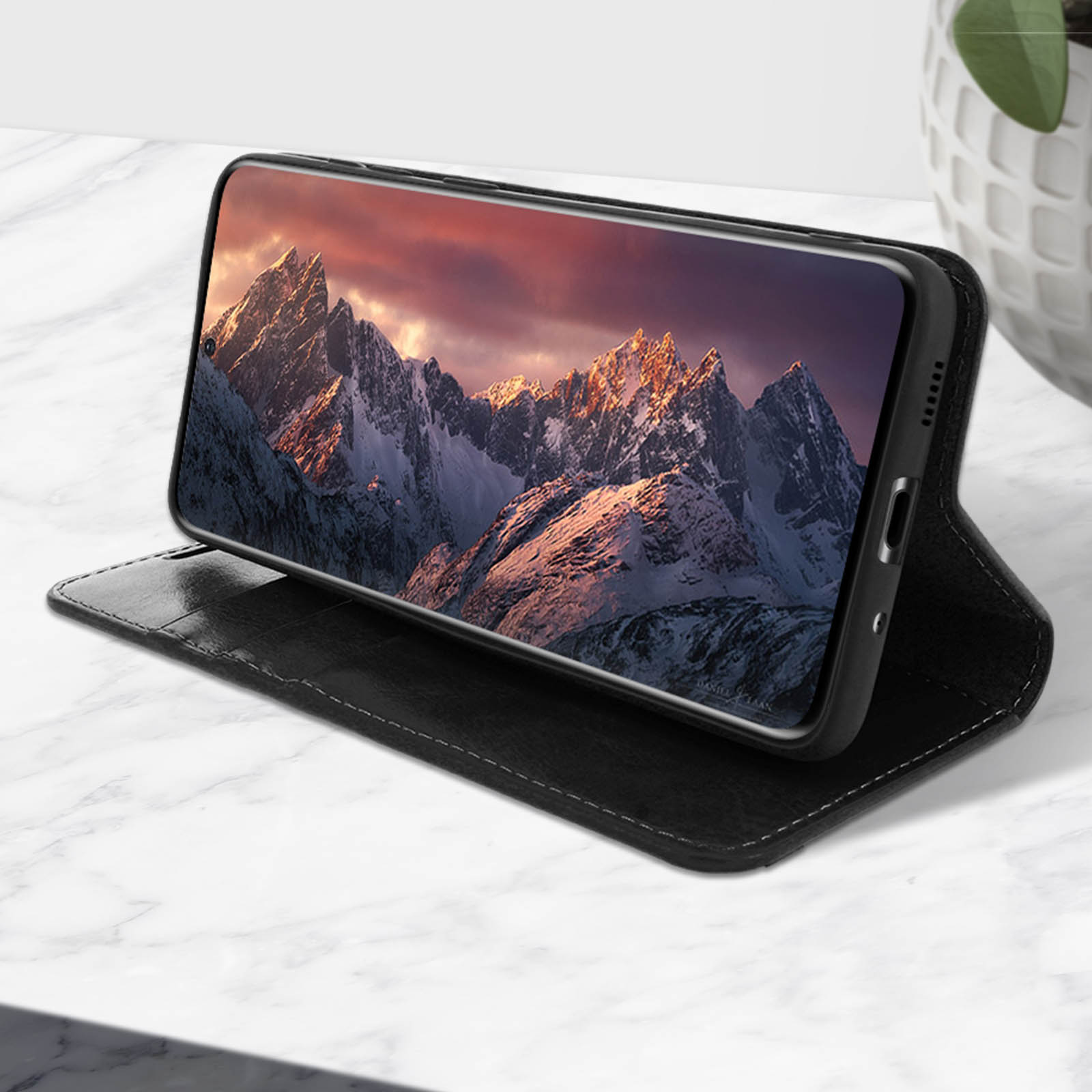 Een telefoon in een zwarte hoes, met een zonsondergang, geopend op een marmeren oppervlak.