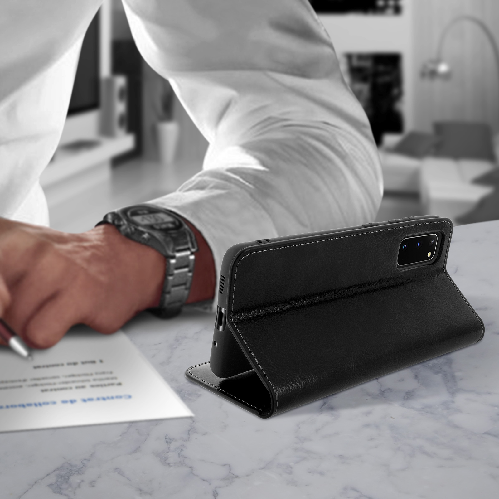 Een zwarte telefoonhoes ligt op een marmeren tafel. Een man schrijft op de achtergrond.