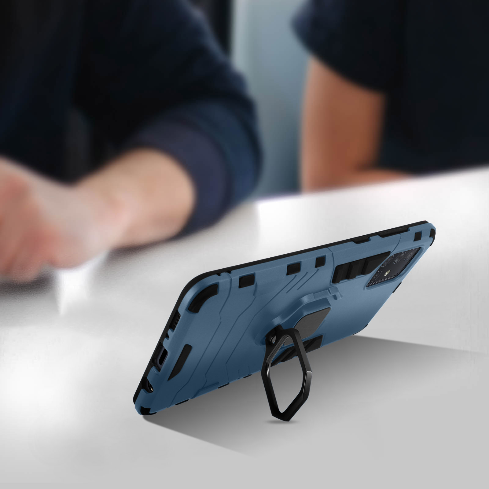 Téléphone bleu avec une coque noire. La coque a un support en anneau. Le téléphone est sur une table blanche.