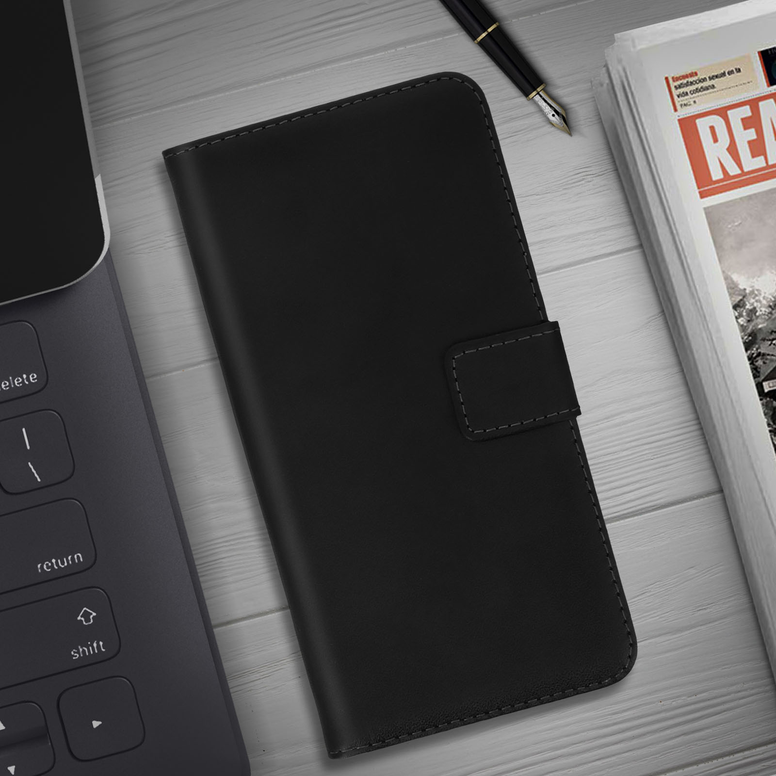 Een zwarte telefoonhoes ligt op een houten tafel met een laptop en een krant. De hoes is gesloten met een sluiting.