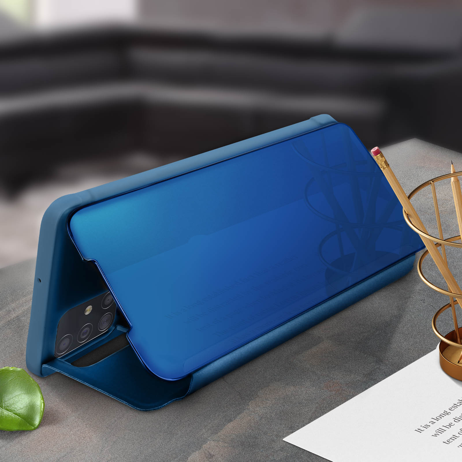 Custodia blu per telefono con copertura a specchio, appoggiata su una scrivania con una matita e una foglia.