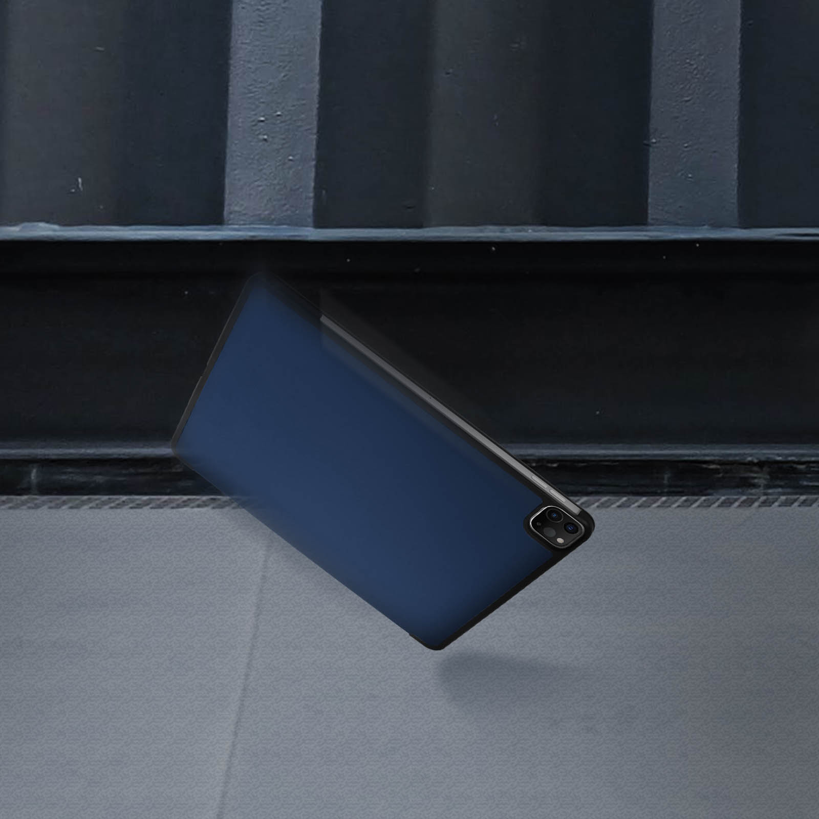 Tablet in custodia blu che cade. Sfondo scuro, mostra i bordi.