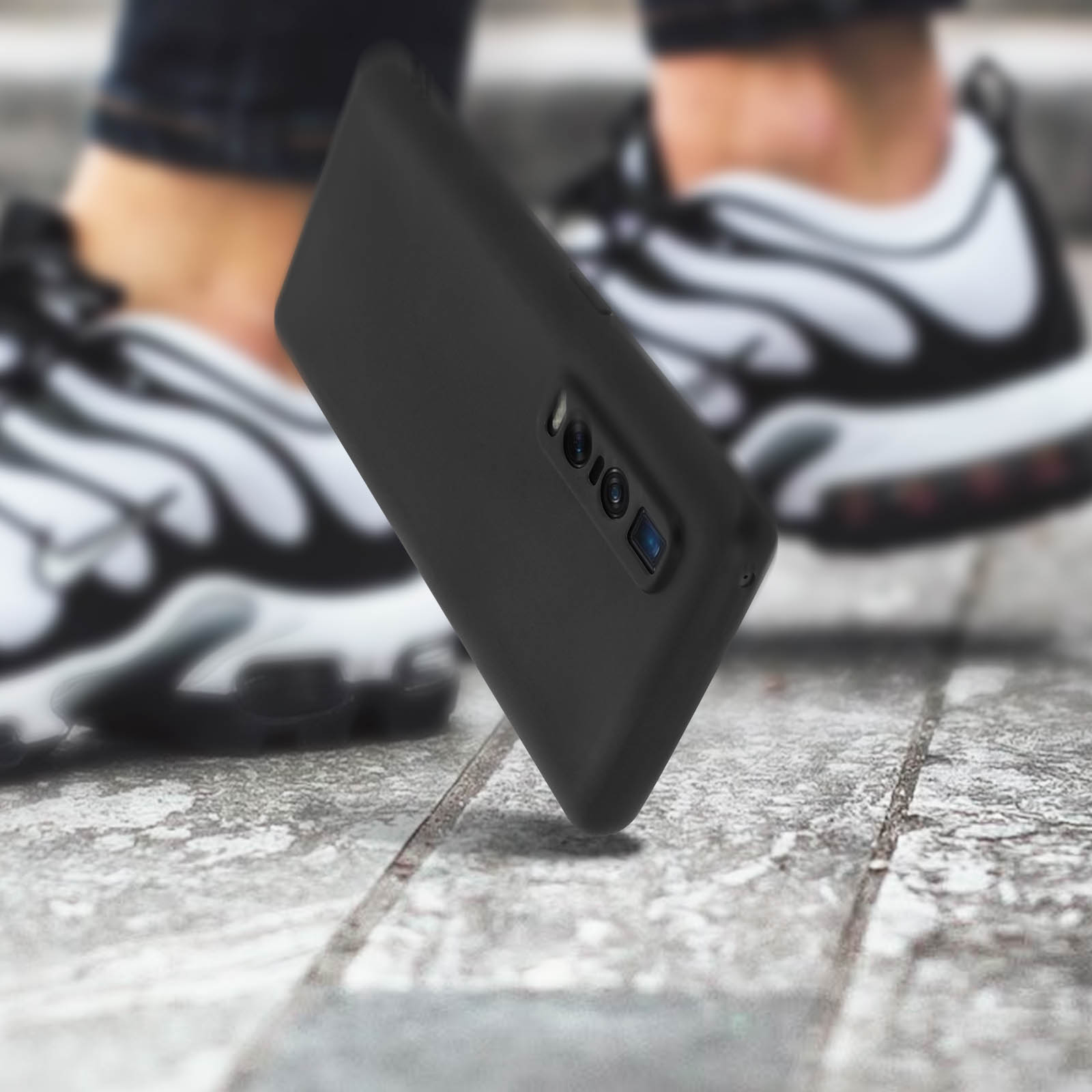 Een zwarte telefoonhoes ligt op een grijs stenen oppervlak. De persoon draagt witte sneakers.