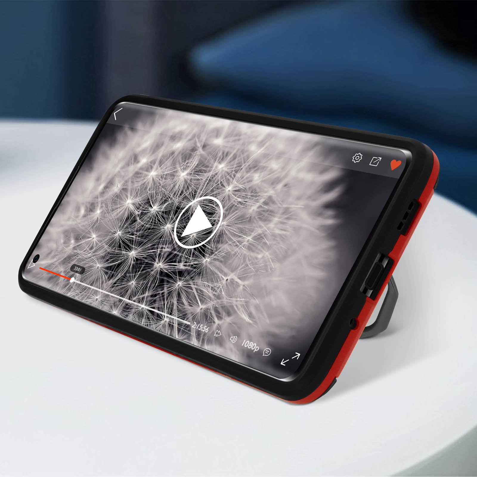 Telefono con custodia rossa che mostra la riproduzione video. Tavolo bianco e sfondo sfocato.