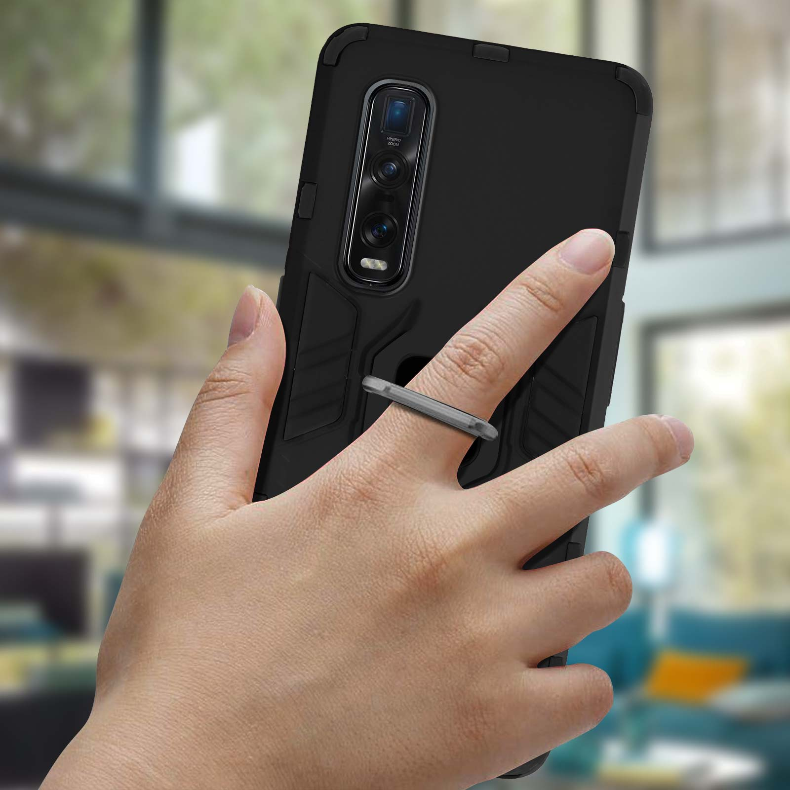 Hand die een zwarte telefoon vasthoudt met een ringhouder, binnenshuis met een wazige achtergrond.