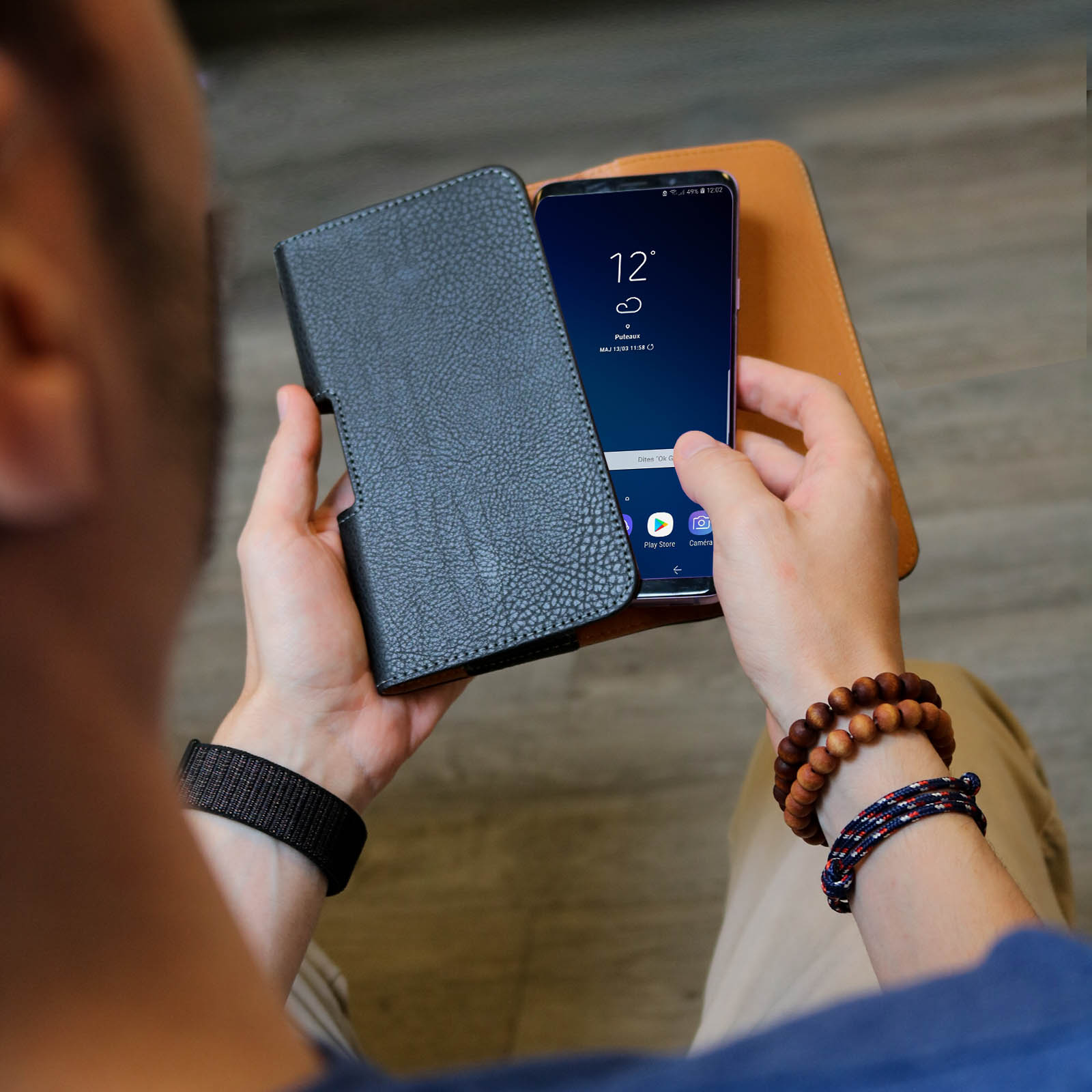 Eine Person hält ein Telefon in einer Hülle. Das Telefon zeigt eine Uhr. Es gibt Armbänder und Uhrenarmbänder.