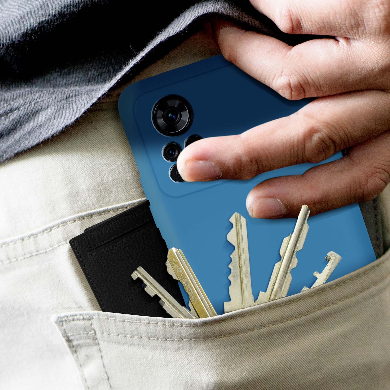 Mano in tasca con telefono, chiavi e portafoglio. Custodia blu visibile. Pantaloni beige.