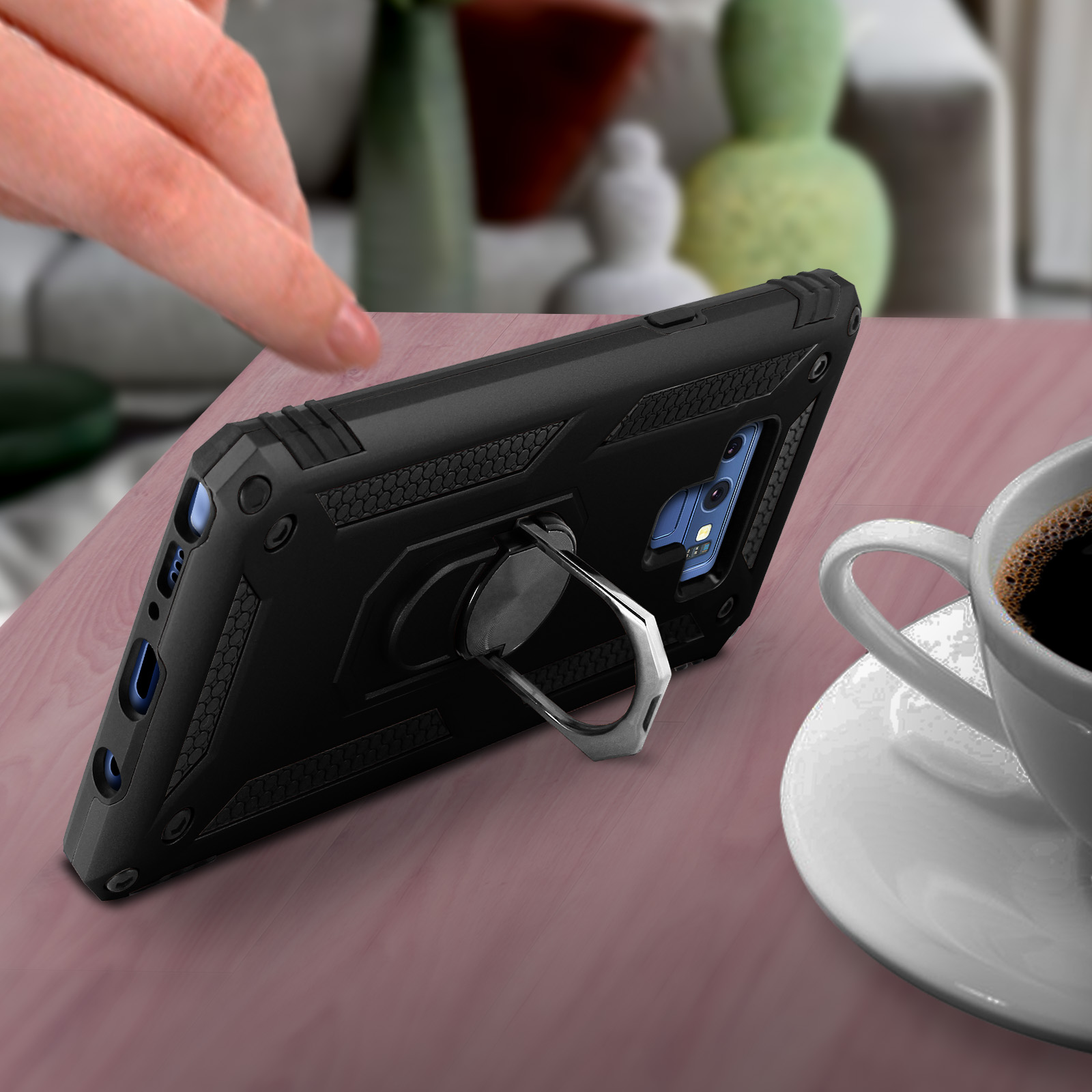 Custodia nera per telefono su una superficie di legno con una tazza di caffè. Una mano si avvicina al telefono.