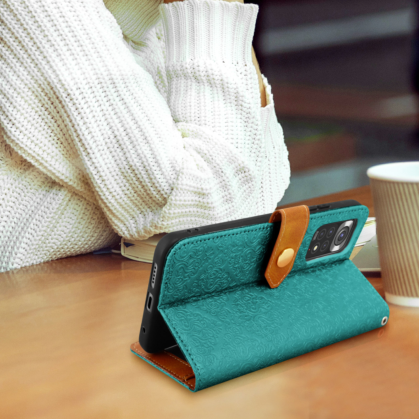 Un téléphone dans un étui vert avec une sangle marron est sur une table en bois.