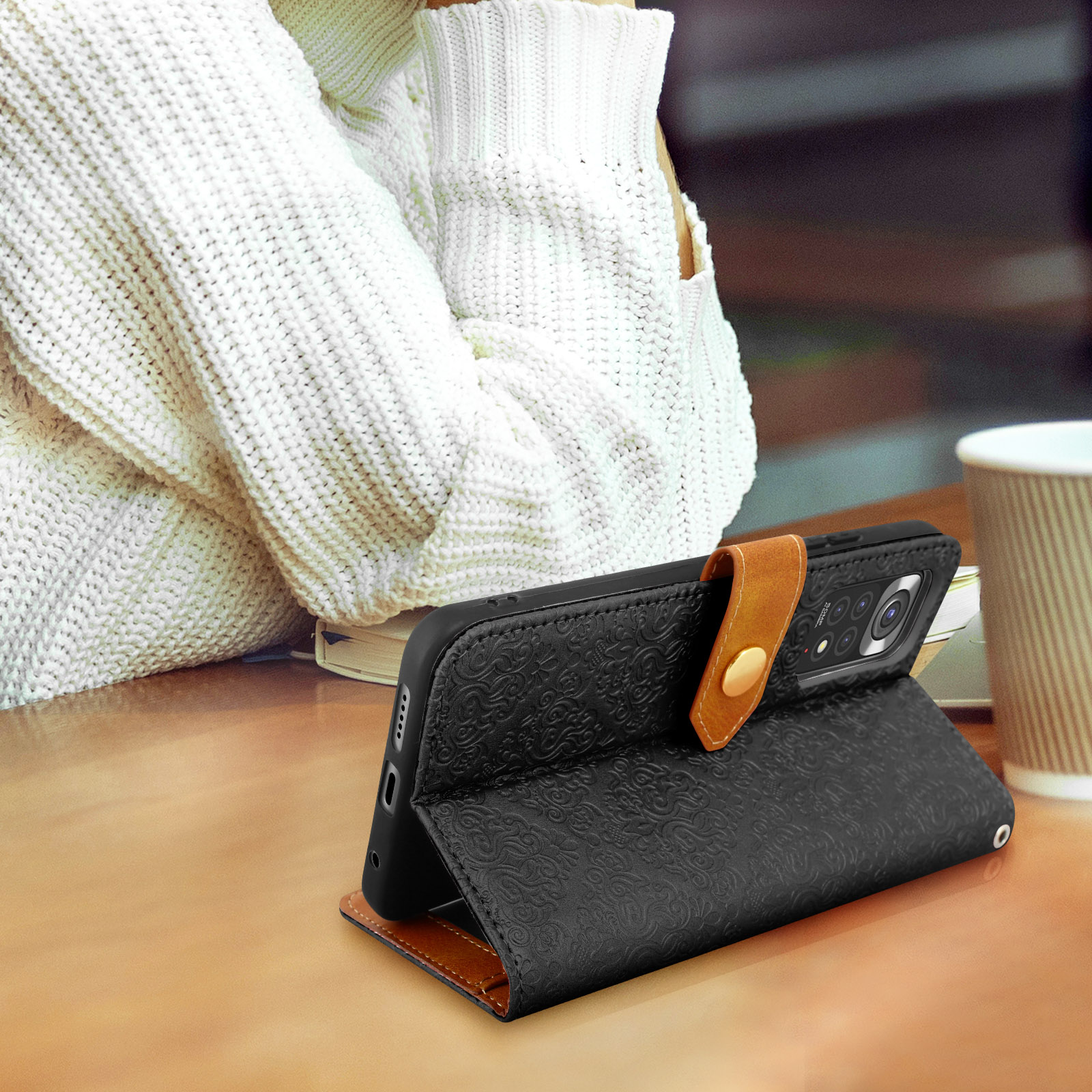 Un téléphone dans un étui noir avec une sangle marron. L'étui a un motif floral.
