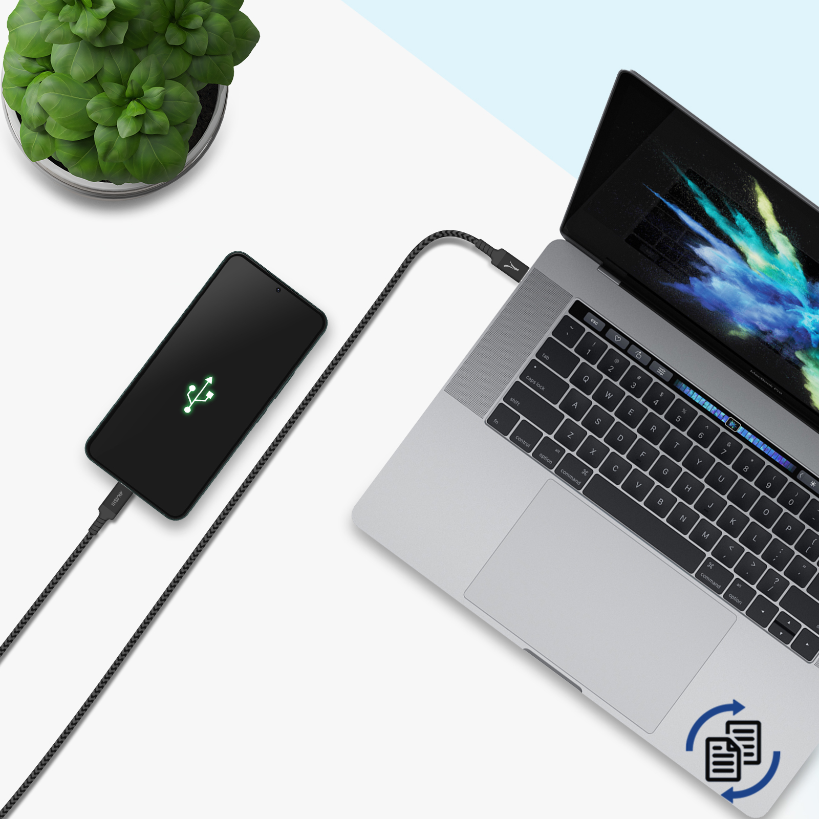 Laptop collegato a un telefono in carica tramite un cavo nero. Pianta verde a sinistra.