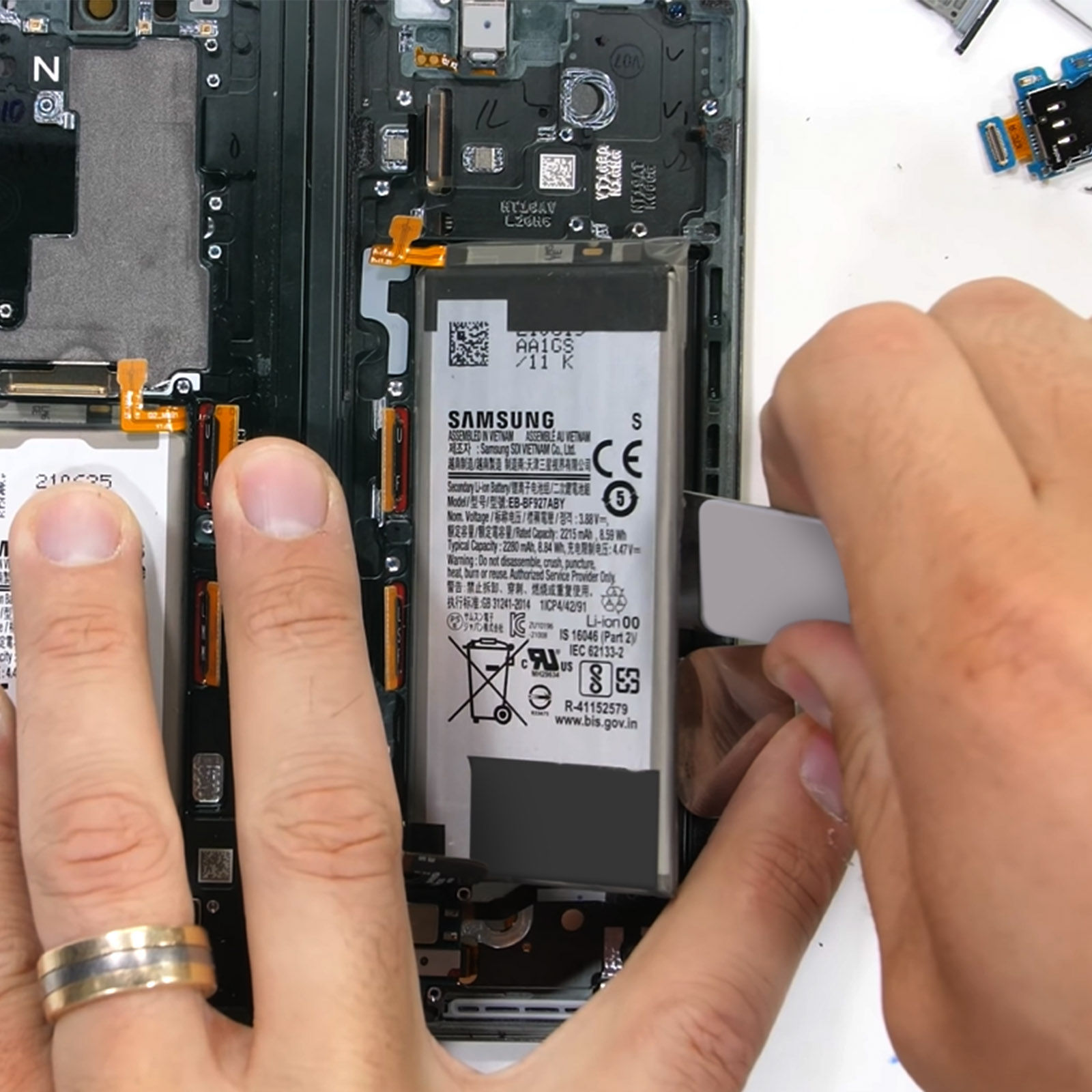 Mains travaillant sur un téléphone démonté. La batterie du téléphone est en train d'être retirée.