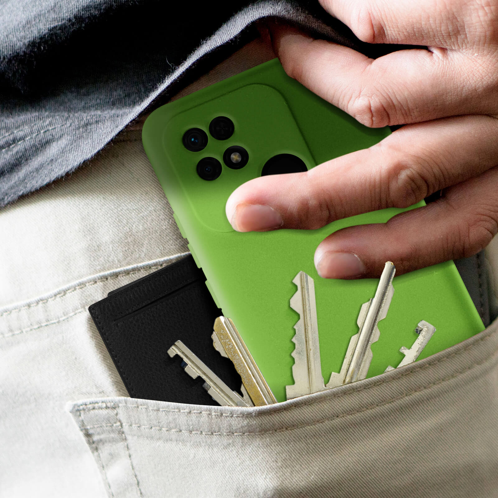 Une main dans une poche tenant une coque de téléphone verte, des clés et un porte-cartes noir.