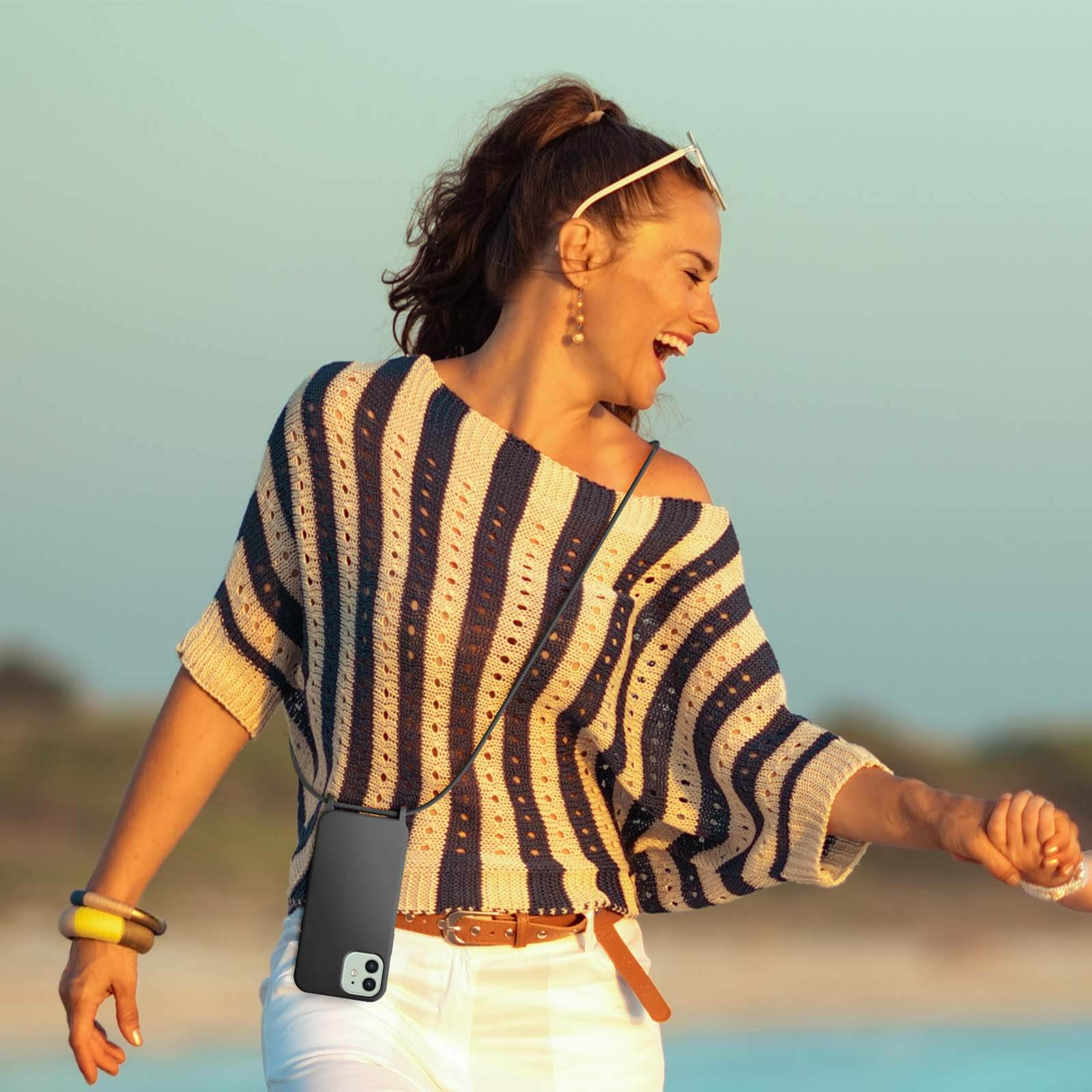 Frau mit gestreiftem Hemd, hält Handy an Lanyard. Hintergrund ist Strand.