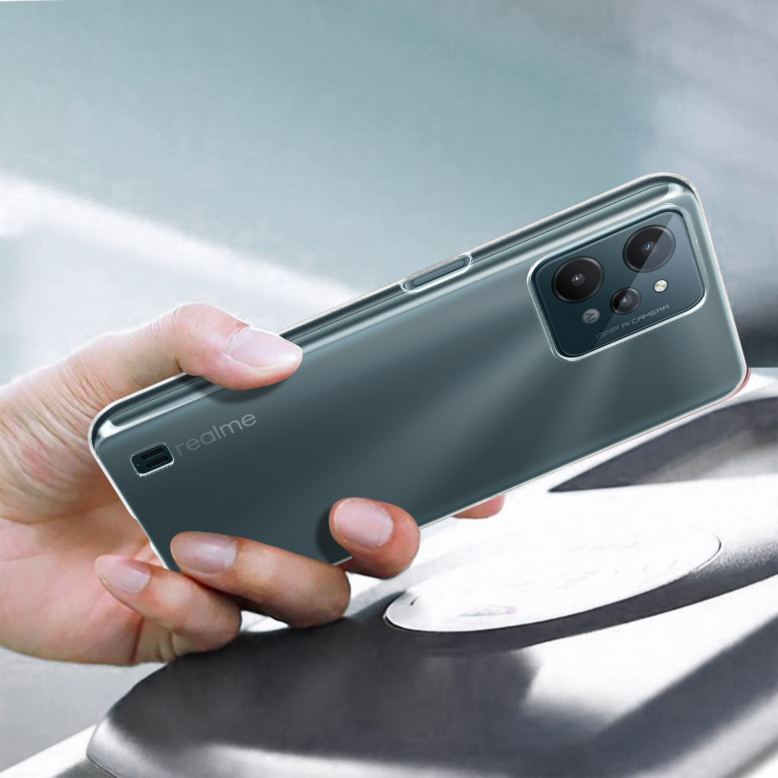 Mano che tiene un telefono in una custodia trasparente, con una fotocamera visibile, su uno sfondo sfocato.