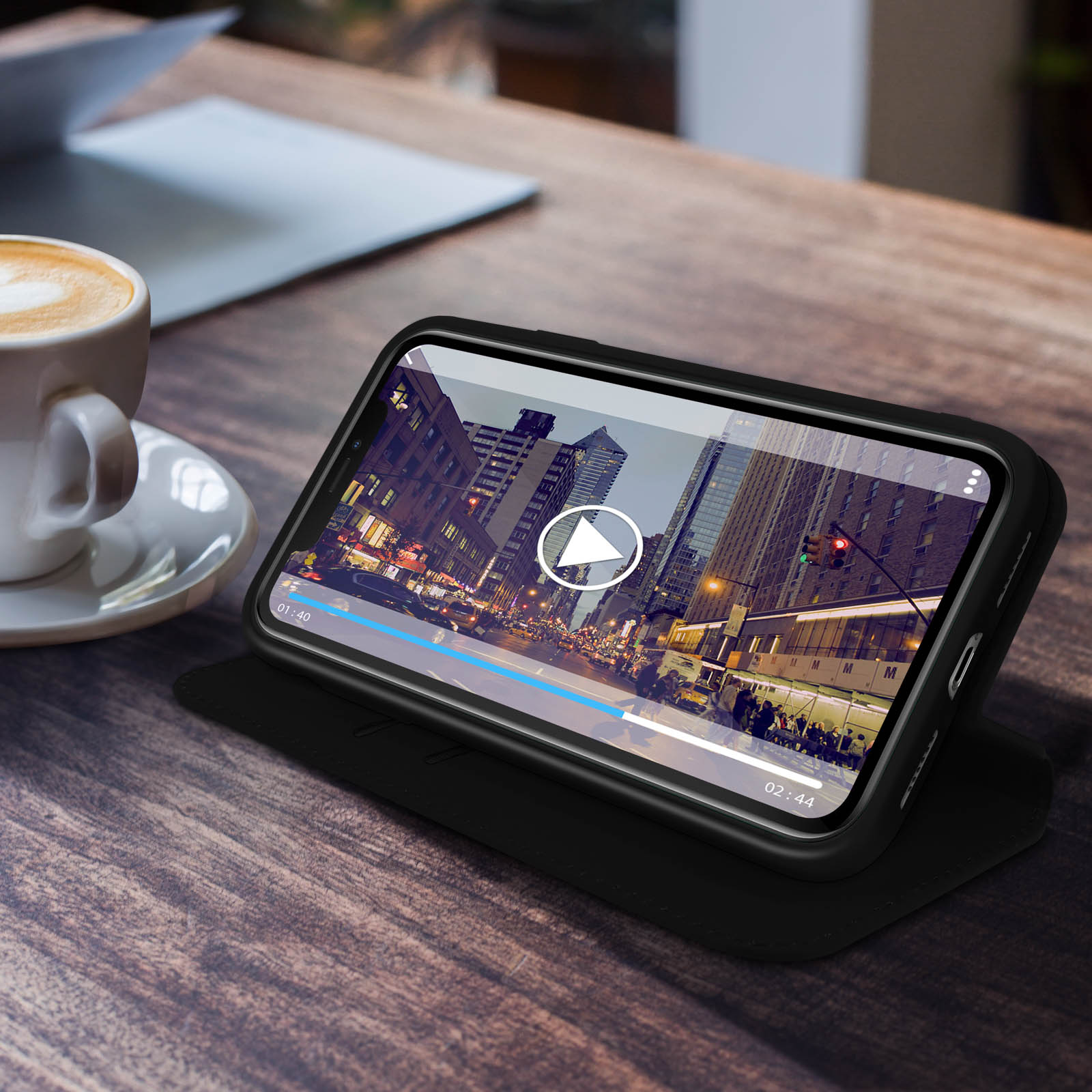 Telefoon in hoes, video afspelen op tafel. Koffie en notitieboek zichtbaar. Stadsgezicht in de video.
