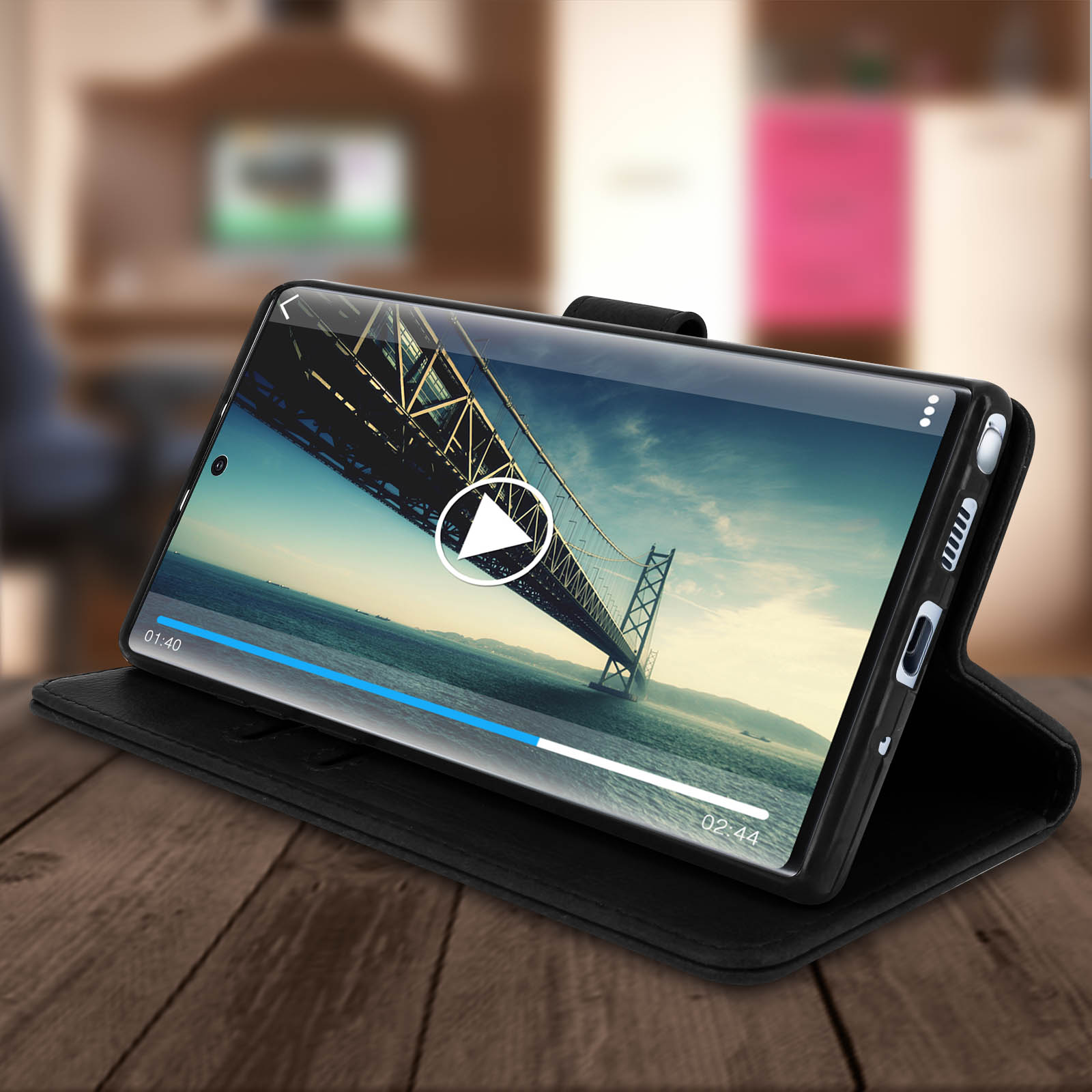 Een telefoon in een hoes, speelt een video van een brug, op een houten tafel.